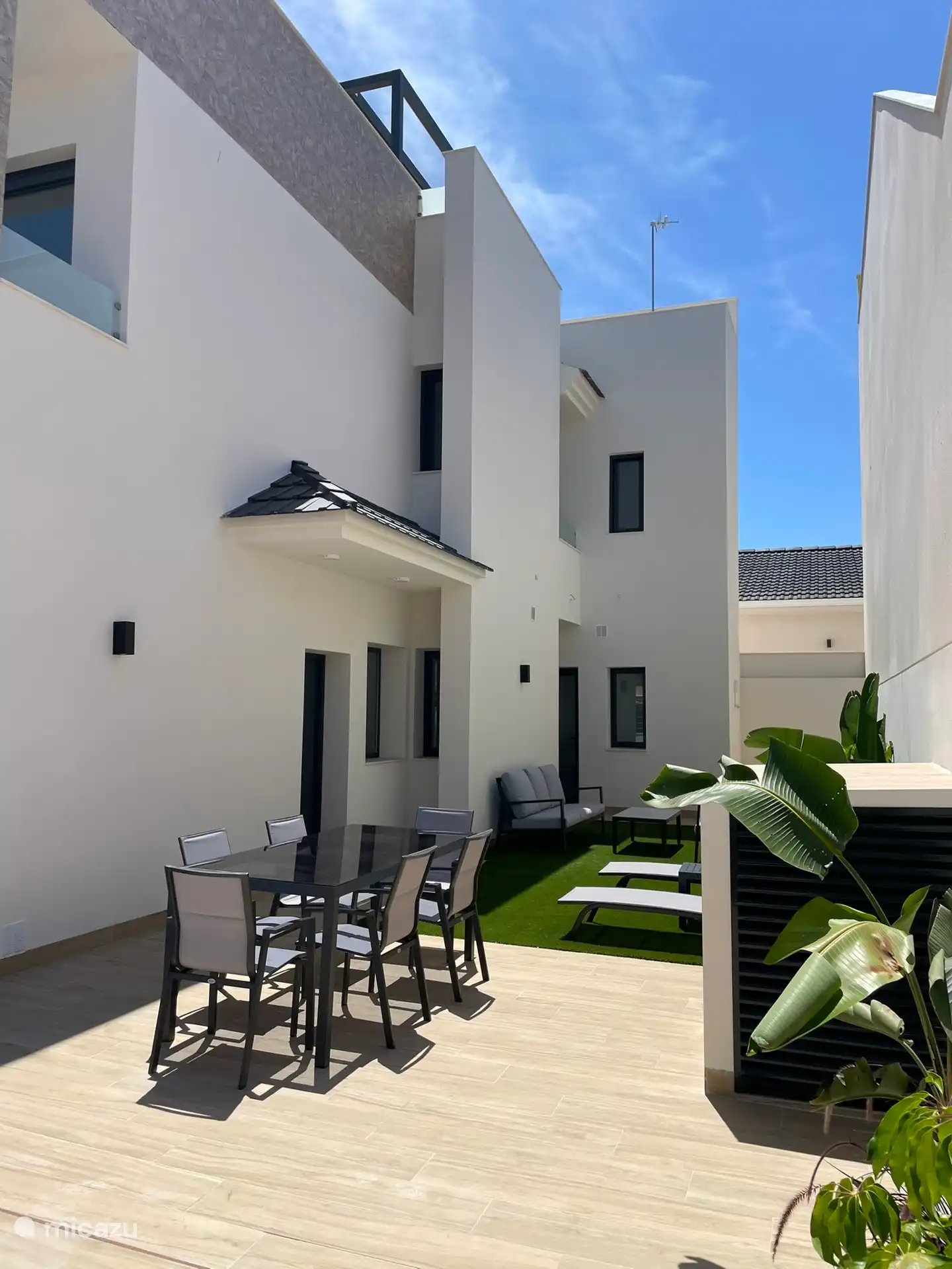Zona exterior con mesa y 6 sillas, 2 tumbonas y un salón.