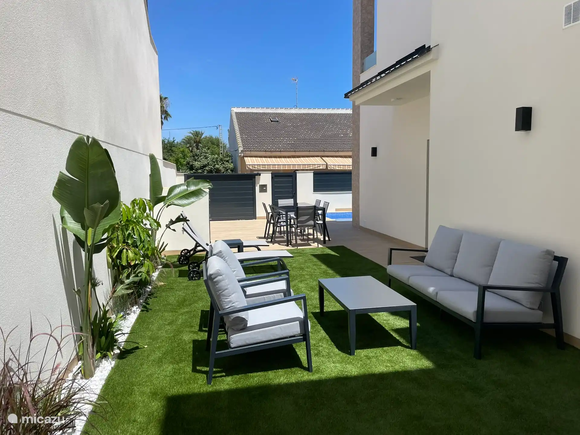 Zona exterior con mesa y 6 sillas, 2 tumbonas y un salón.
