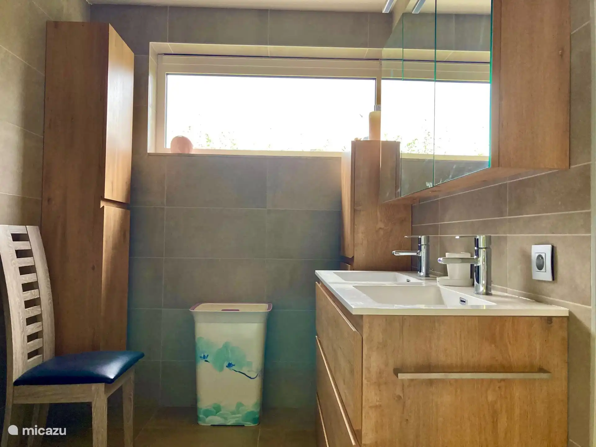 Badkamer met dubbel lavabomeubel , spiegelkast en twee hangkasten met handdoeken, linnenmand en stoel