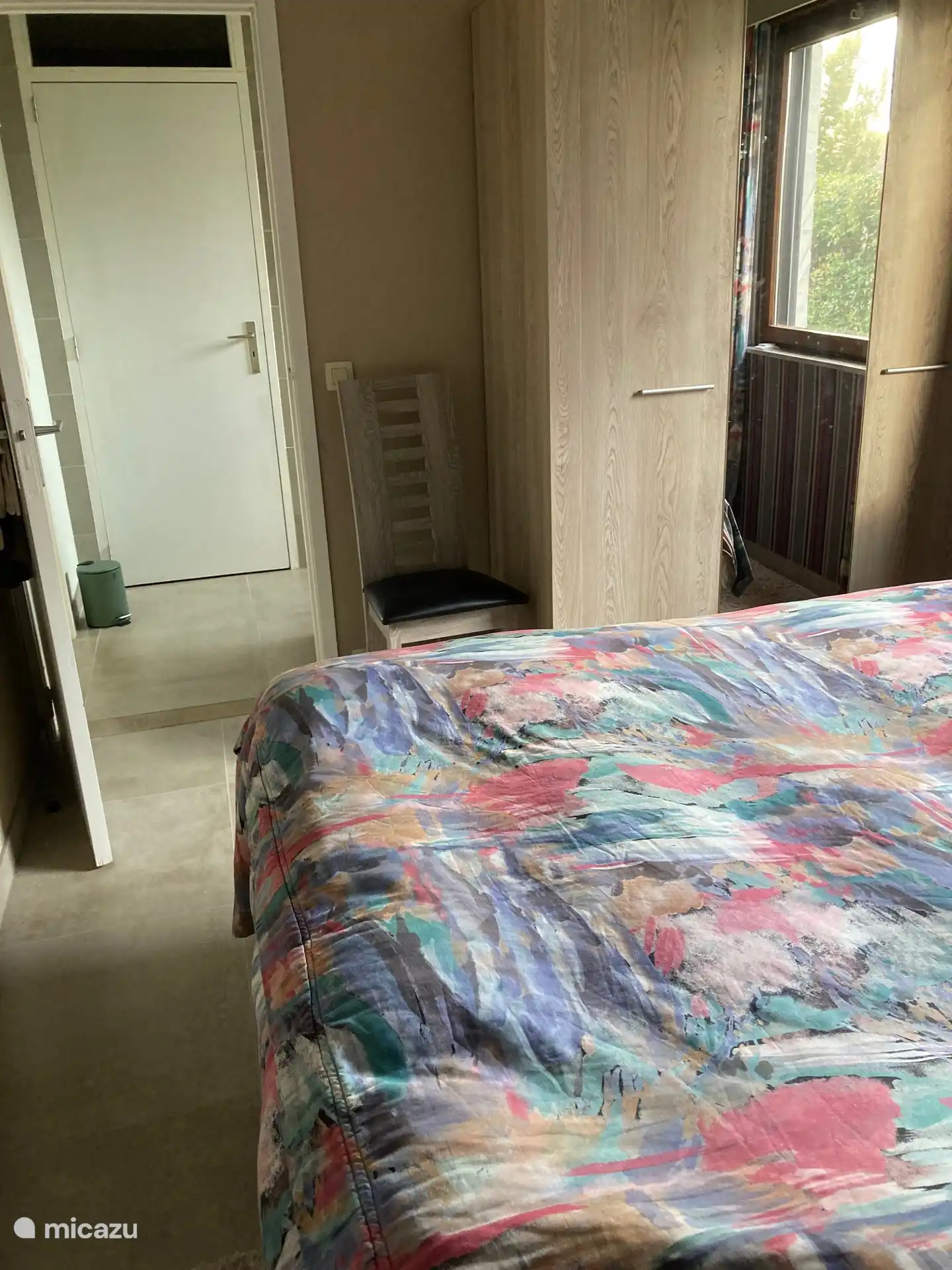 slaapkamer met bed, kleerkast en toegang tot badkamer met rechtover toegang tot apart toilet.