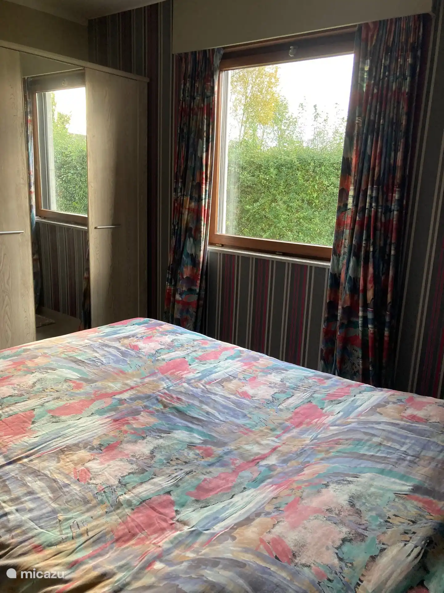 slaapkamer met kleerkast en raam met uitzicht op tuin met elektrisch rolluik