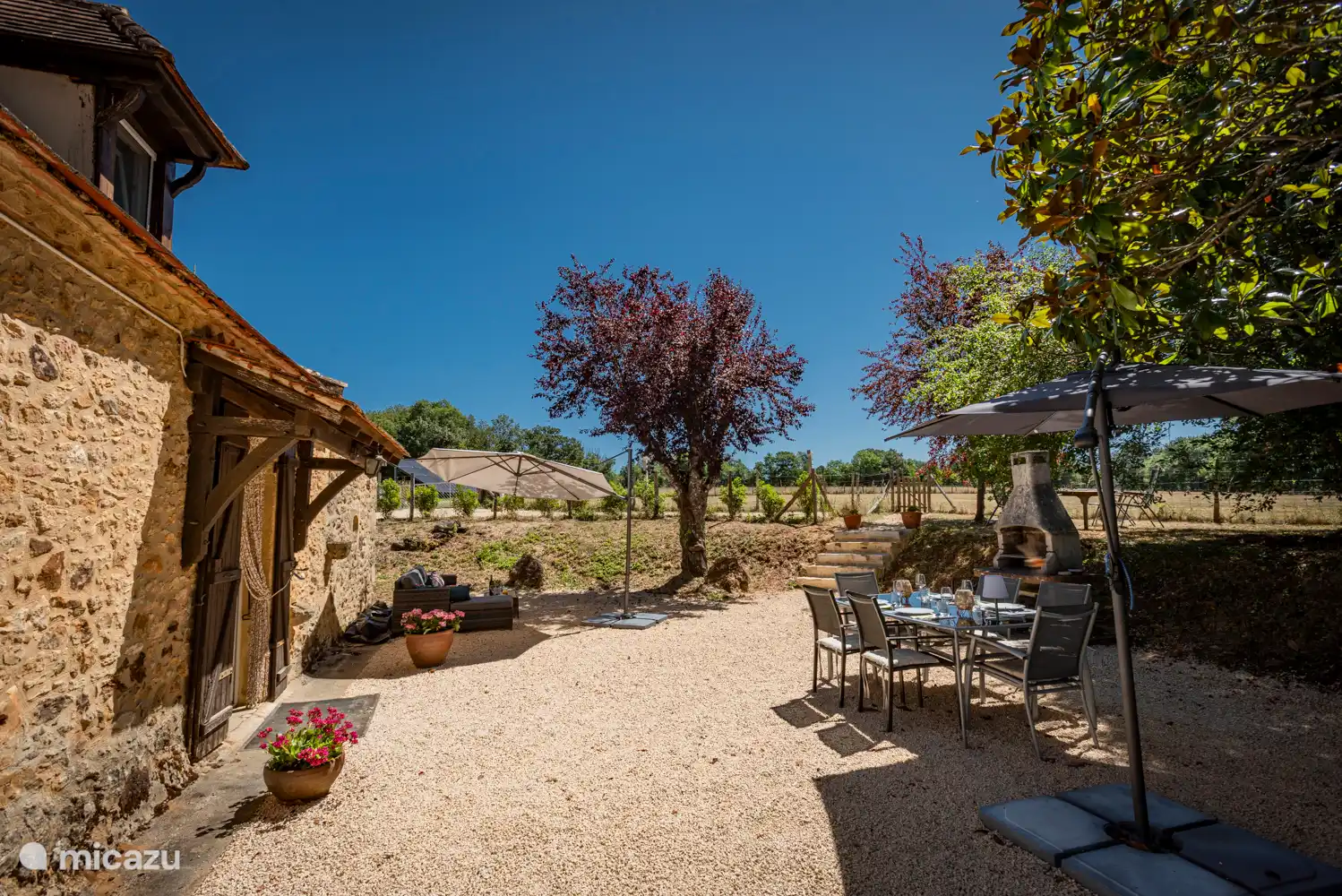 Geräumige Terrasse mit Schatten und Sonnenbereichen, Lounge-Sofa, Esstisch und Grill. Blick auf die Felder und Obstbäume.