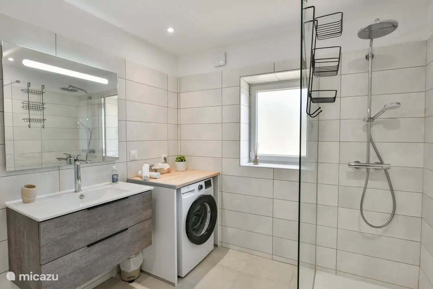 Geräumiges Badezimmer mit Waschbecken, beleuchtetem Spiegel, großer Regendusche, Waschmaschine, Heizung, Belüftung und Fliegengitter.