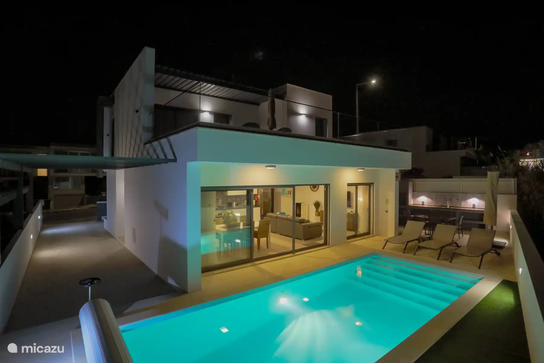 Villa Caldara la nuit, baignée d’une lumière douce et atmosphérique. La villa dispose de grandes portes et fenêtres en verre, créant une connexion transparente entre l’espace de vie intérieur et extérieur.