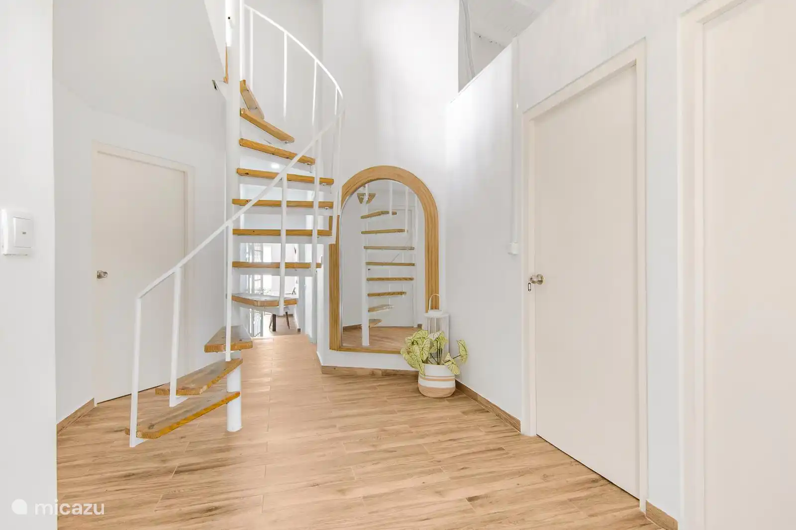 La moderna escalera de caracol de madera y color blanco conecta el primer piso con el segundo, realzada por un gran espejo y detalles decorativos que aportan luminosidad y elegancia al espacio.