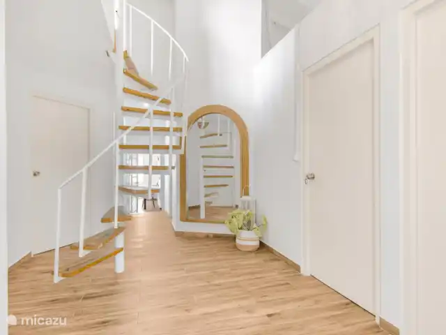 SOMETHING ELS huren in Curaçao, Banda Ariba (oost), Marie Pampoen - vakantiehuis Una moderna escalera de caracol de madera y color blanco conecta el primer piso con el segundo, realzada por un gran espejo y detalles decorativos que aportan luminosidad y elegancia al espacio.