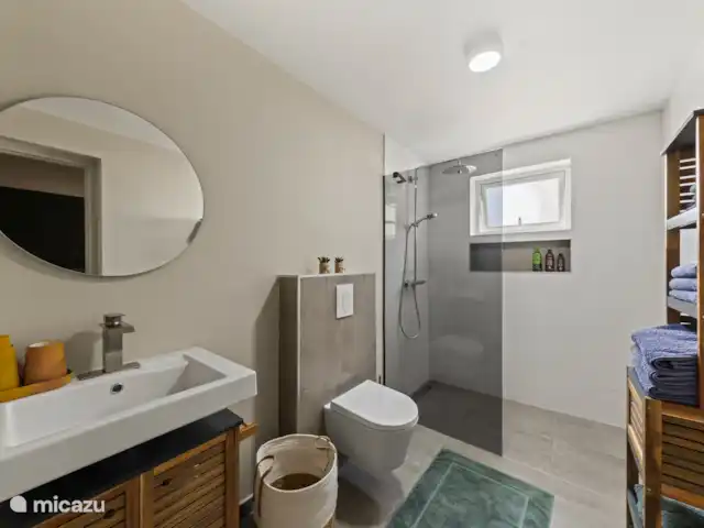 Appartement Mambo Beach | Curaçao, Banda Ariba (est), Bapor Kibra - appartement La salle de bains est élégamment meublée avec une douche moderne, des toilettes flottantes, un lavabo avec miroir et des serviettes Walra douces et un tapis de bain.