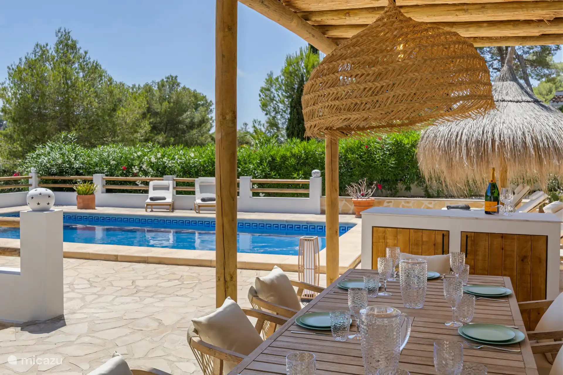 Pérgola junto a la piscina con una amplia mesa de comedor con cocina exterior