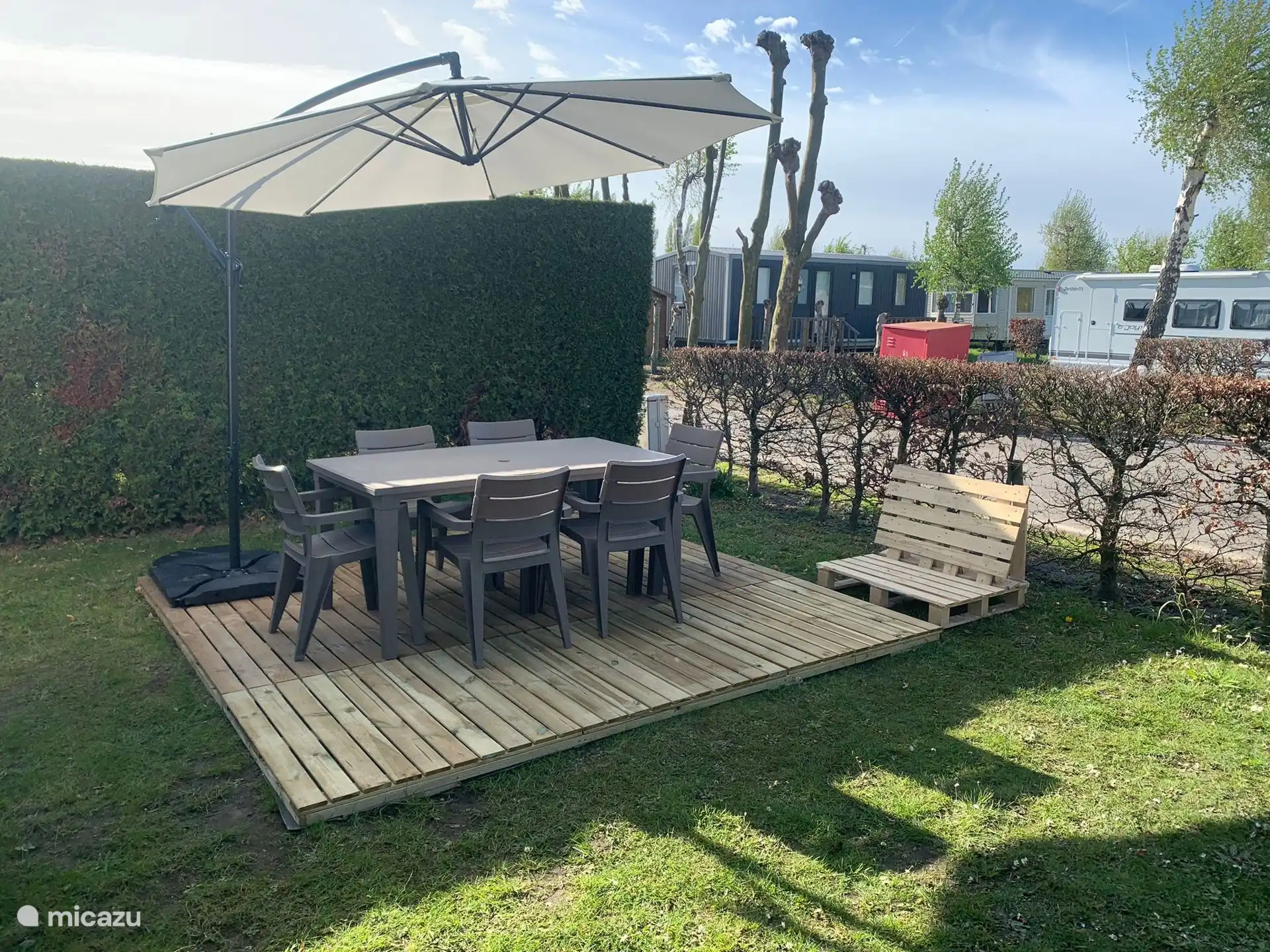 Pequeña terraza frente al chalet con mesa de jardín, seis sillas y sombrilla