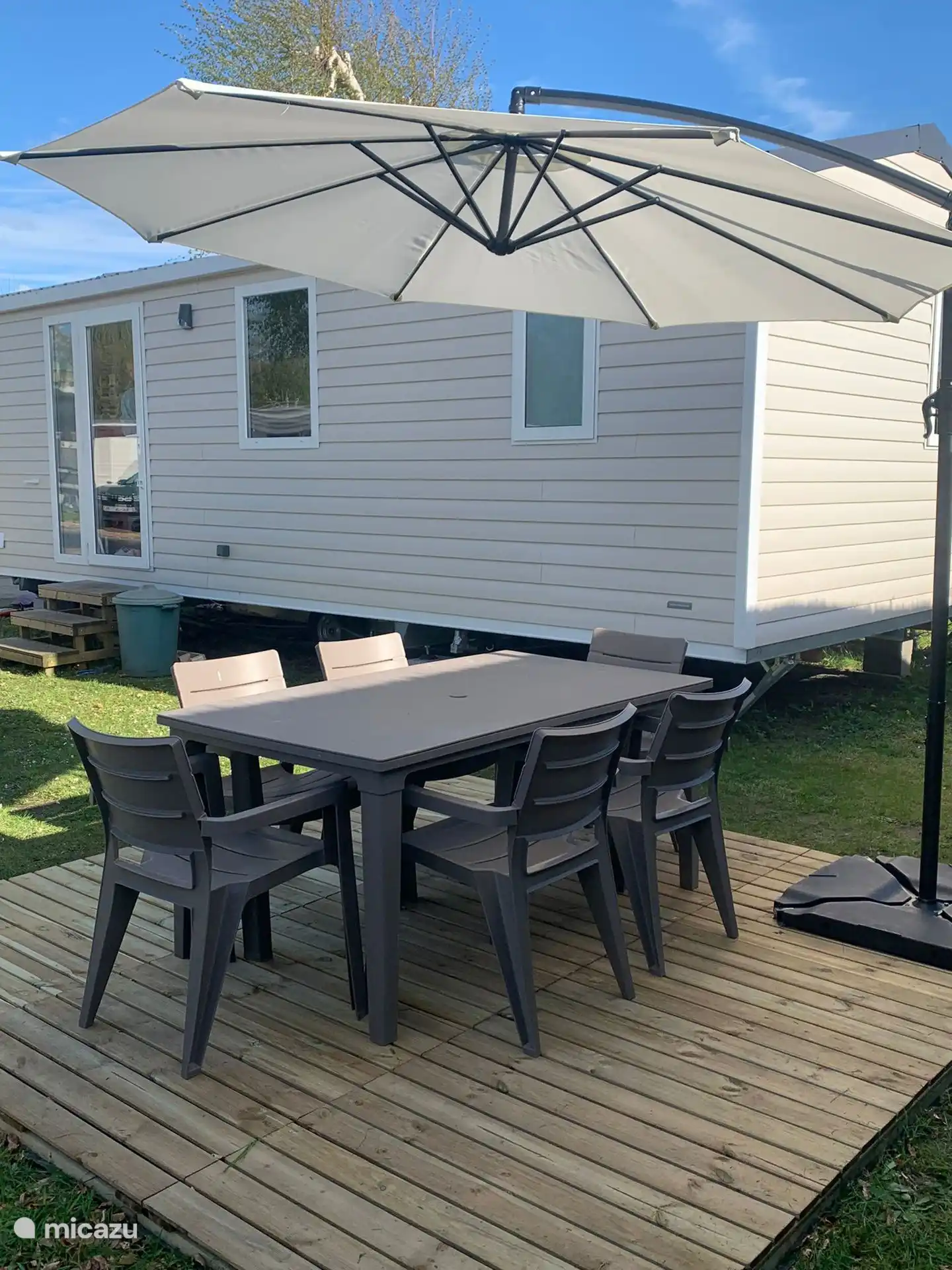 Pequeña terraza frente al chalet con mesa de jardín, seis sillas y sombrilla
