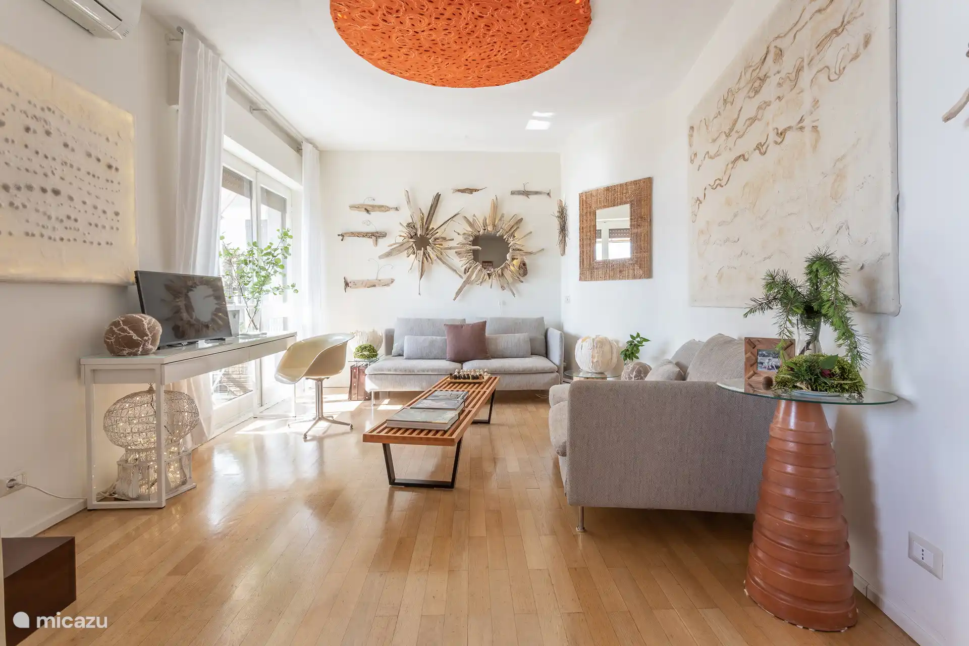 Luminoso salón con dos sofás, escritorio, Smart TV, aire acondicionado, y acceso a balcón y terraza a través de cuatro escalones.