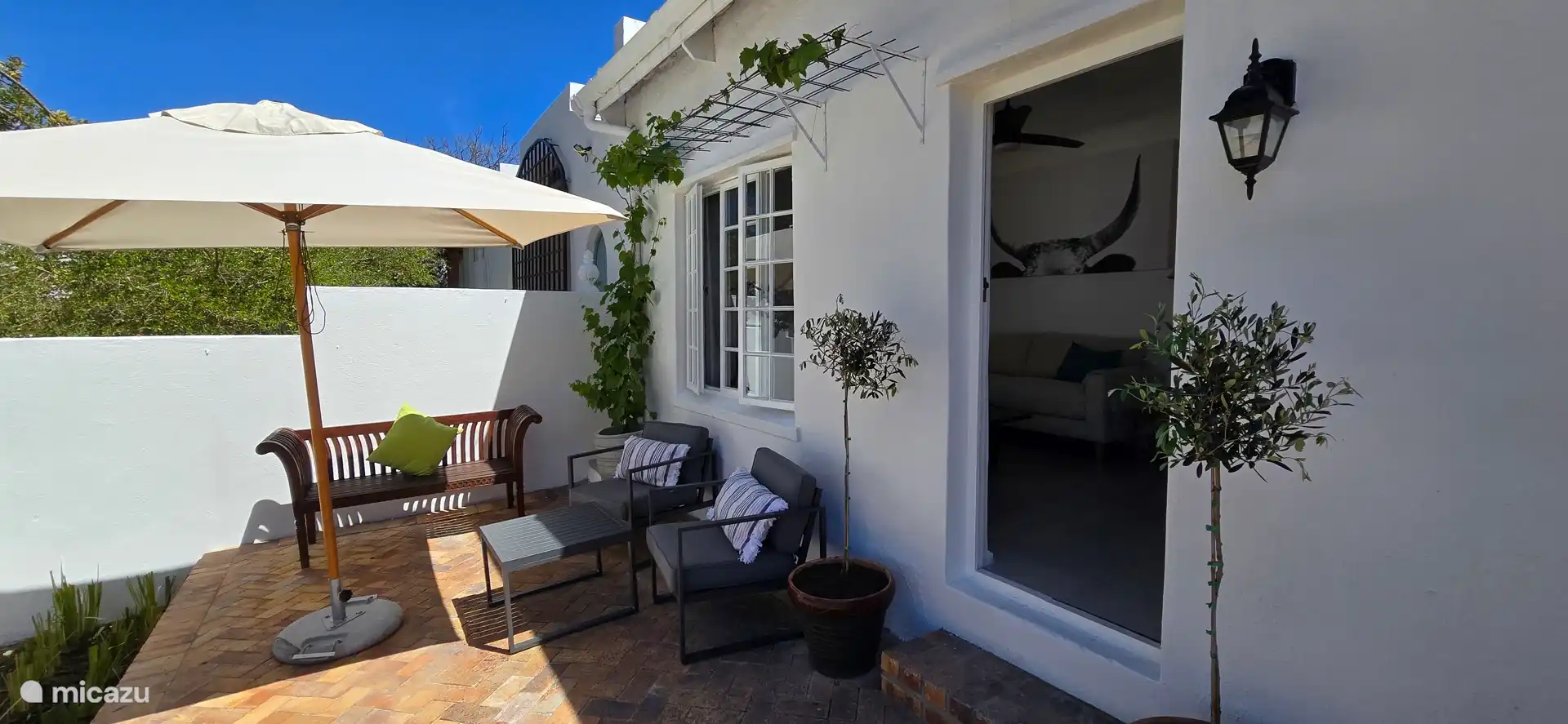 Gemütliche Sonnenterrasse mit einem 2-Sitzer-Sofa aus Teakholz, zwei Terrassenstühlen mit Beistelltisch und Sonnenschirm