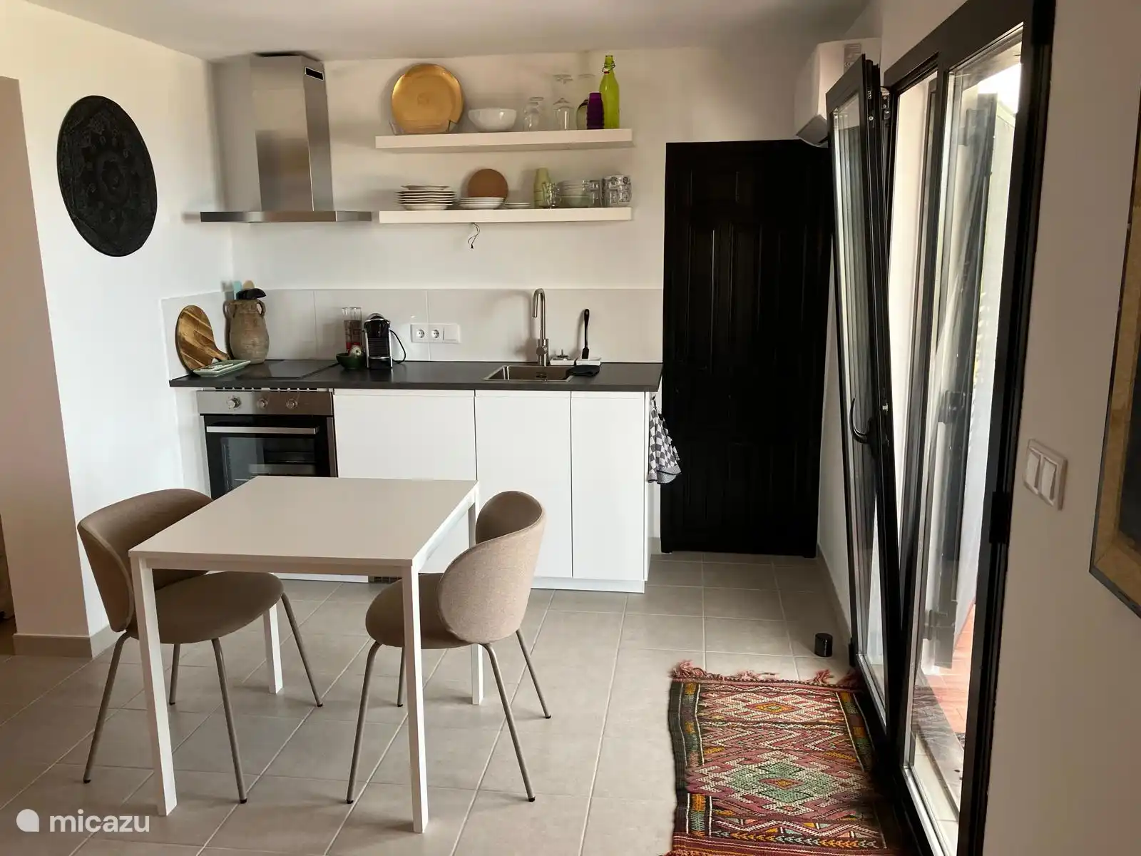 Keuken met deur naar badkamer en eettafel met 2 stoelen. En 2 openslaande deuren naar het balkon. 