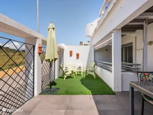 Location de Vacances Espagne, Costa del Sol, Mijas Costa, appartement - Sense-sol Terrasse sud-ouest prise sous un angle différent avec table pour 6 personnes, coin salon partiellement couvert sur gazon artificiel. Accès par le salon, la chambre principale et les escaliers à la troisième chambre et au parking privé.