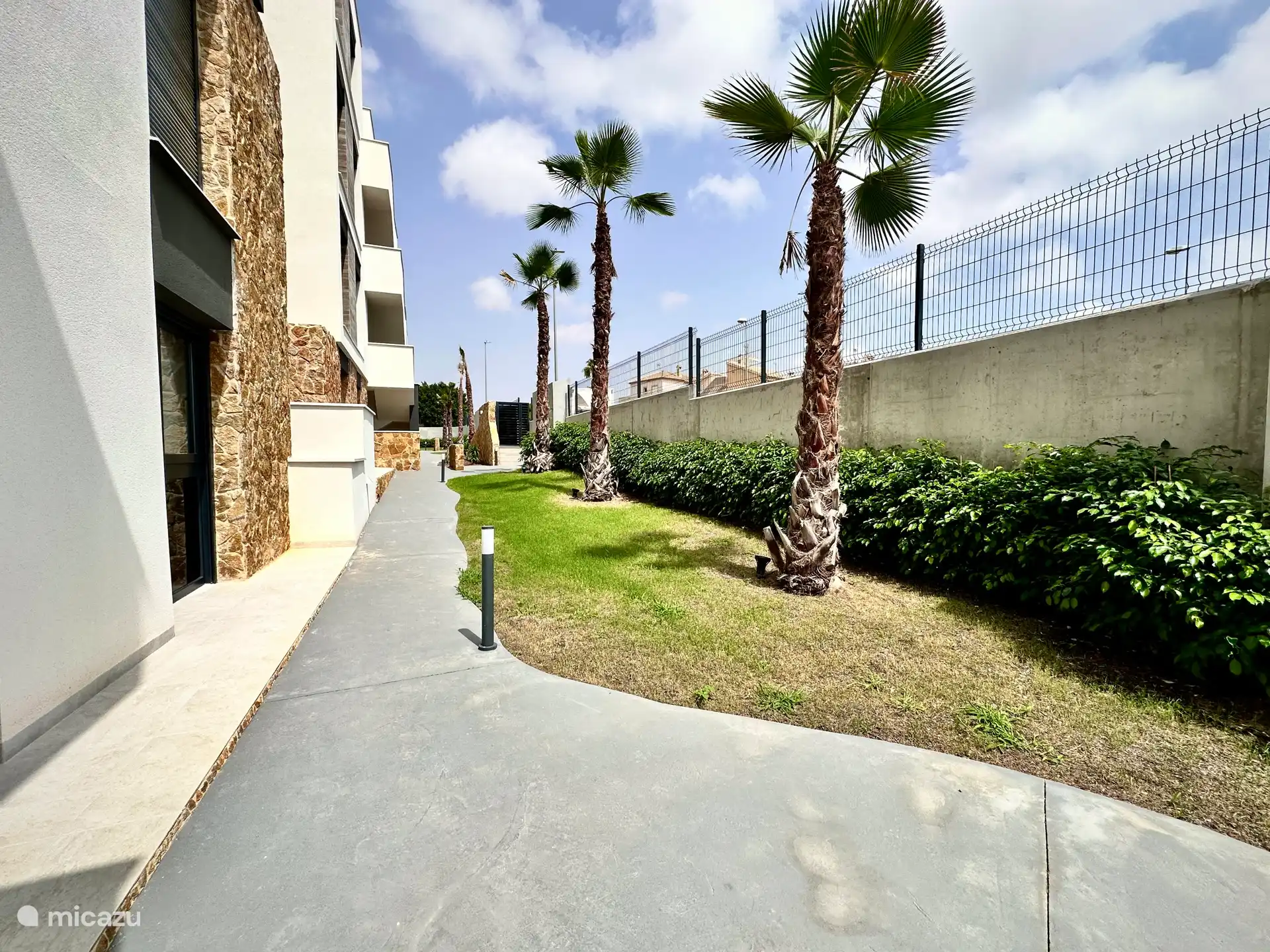 Entree met verzorgde wandelpaden met palmbomen en groen rondom het complex. 