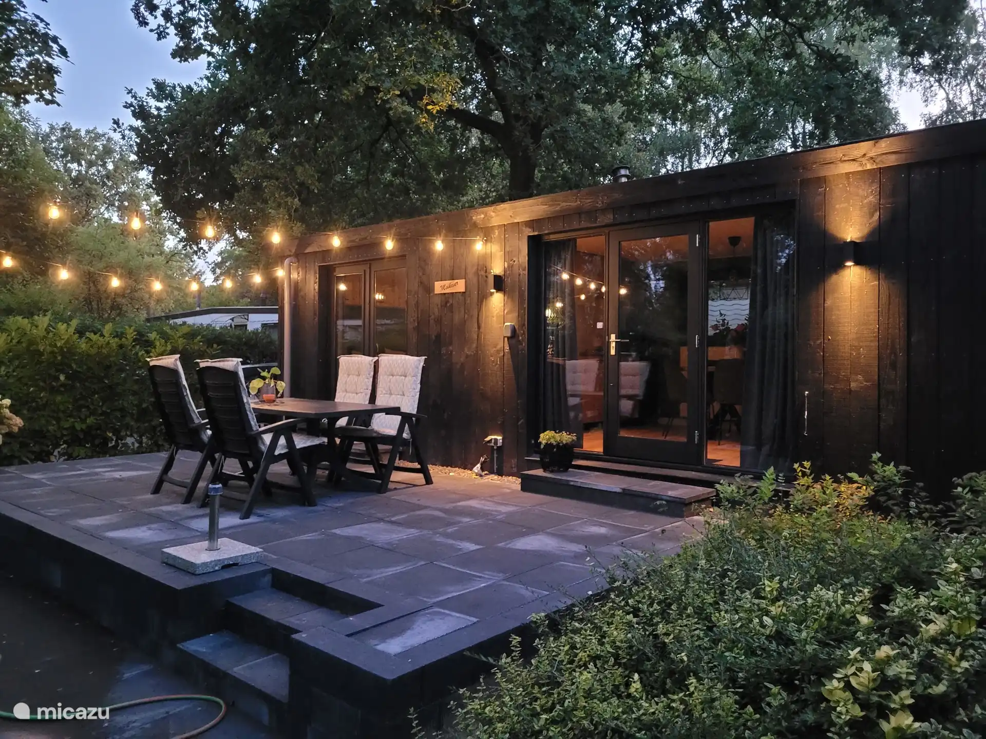 Der Außenbereich des Ferienhauses bei Nacht. Es gibt eine erhöhte Terrasse mit Gartengarnitur und attraktiver Beleuchtung.