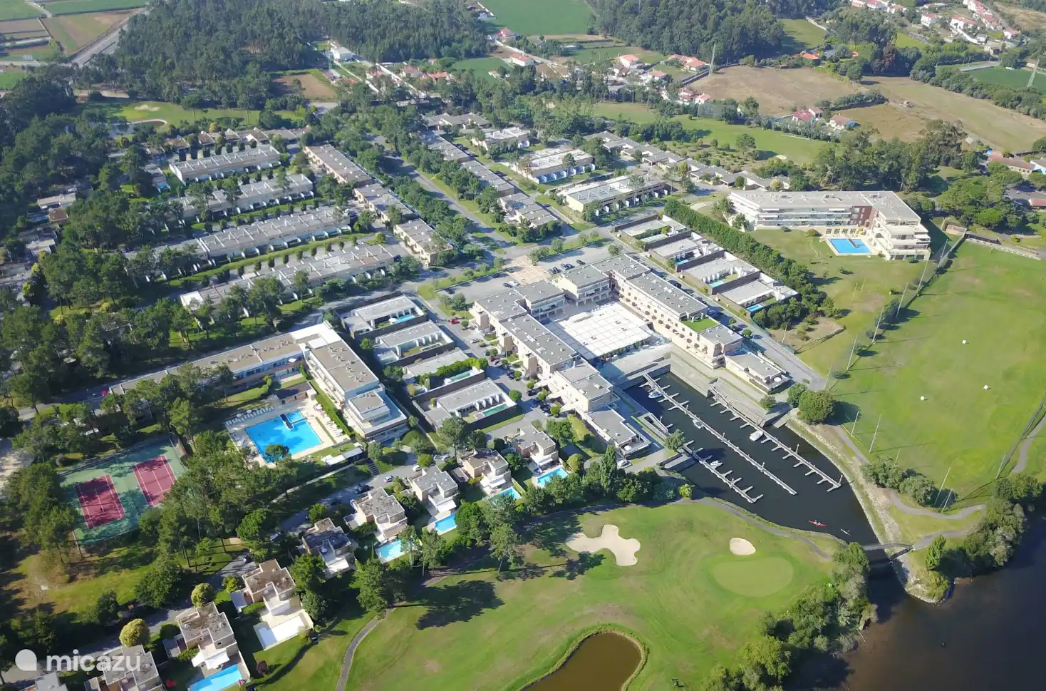 Atemberaubende Luftaufnahme der luxuriösen Eigentumswohnung mit den eleganten Häusern, Tennisplätzen, dem Yachthafen und dem einladenden Swimmingpool, der von üppigem Grün umgeben ist.