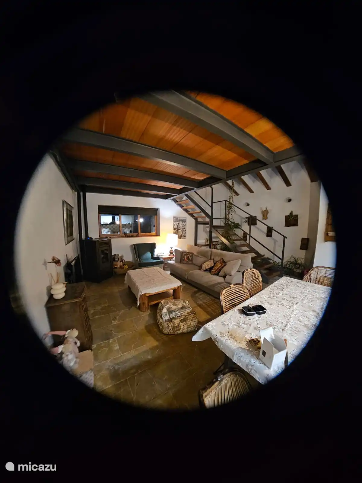 Woonkamer en eetkamer, met de trap aan de achterkant die overdag wordt verlicht door natuurlijk licht dat van rechts binnenkomt, omdat er een glazen dak is en er dus planten in deze ruimte staan. 