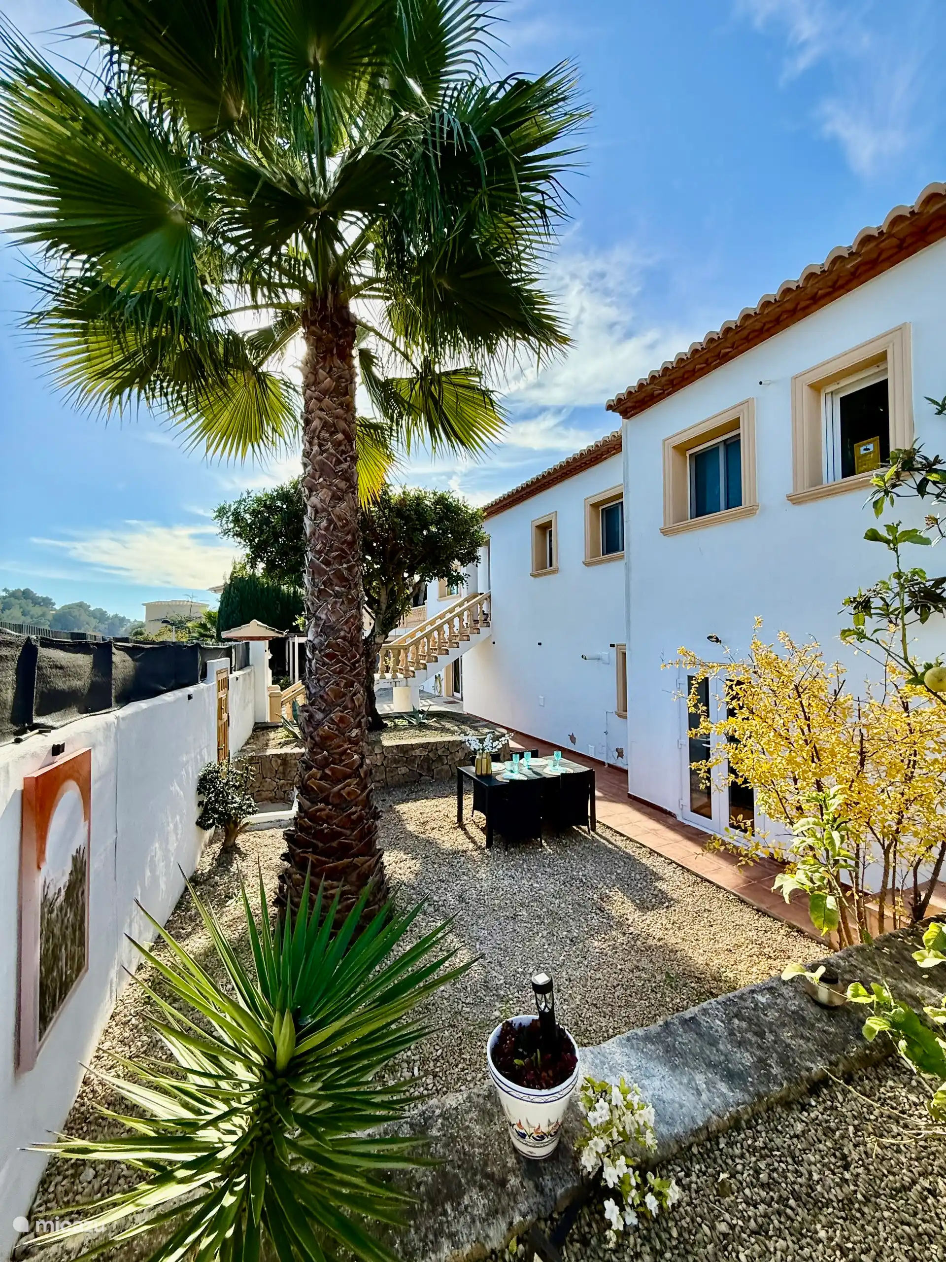 Jardin méditerranéen privé avec table à manger, chaises longues et parasol.