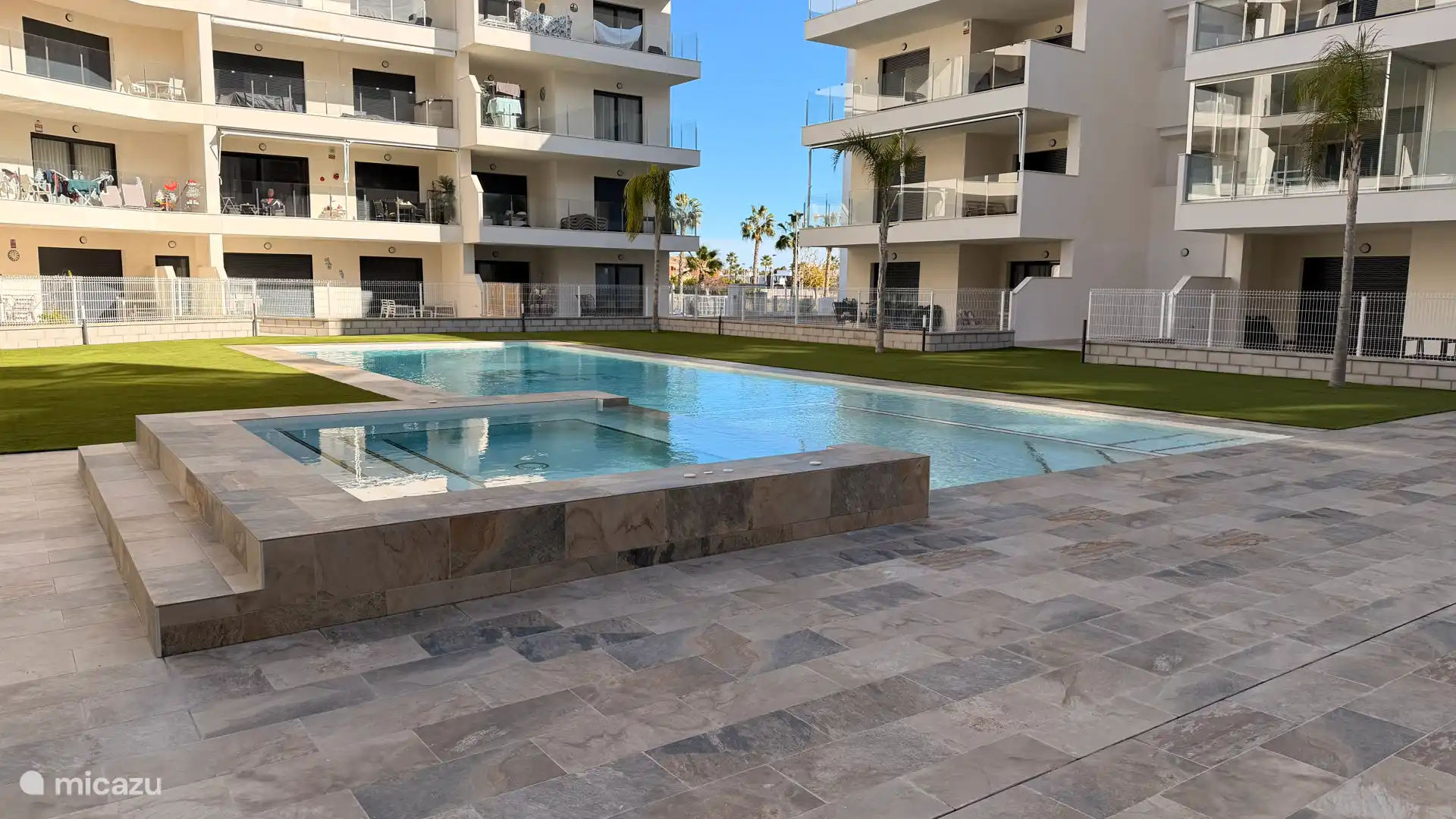 Het modern zwembad met jacuzzi en rondom voorzien van tegels of kunstgras.