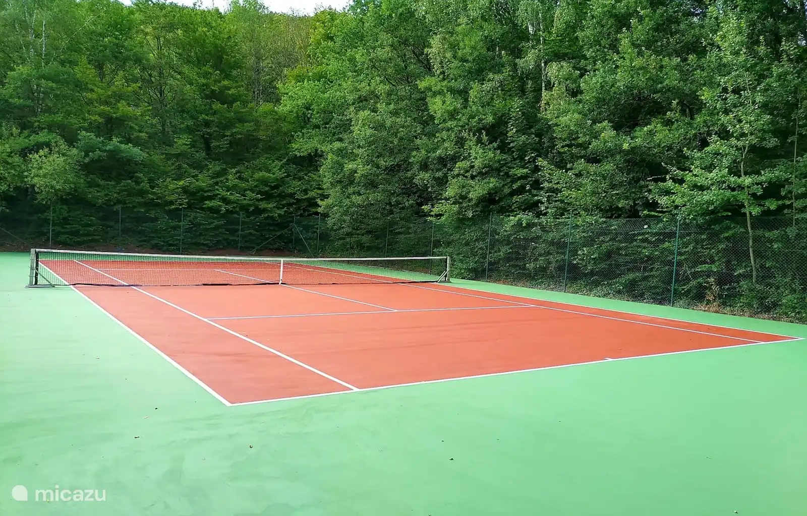 Spielen Sie ein entspanntes Match auf diesem ruhigen Tennisplatz, umgeben von Bäumen und frischer Luft.