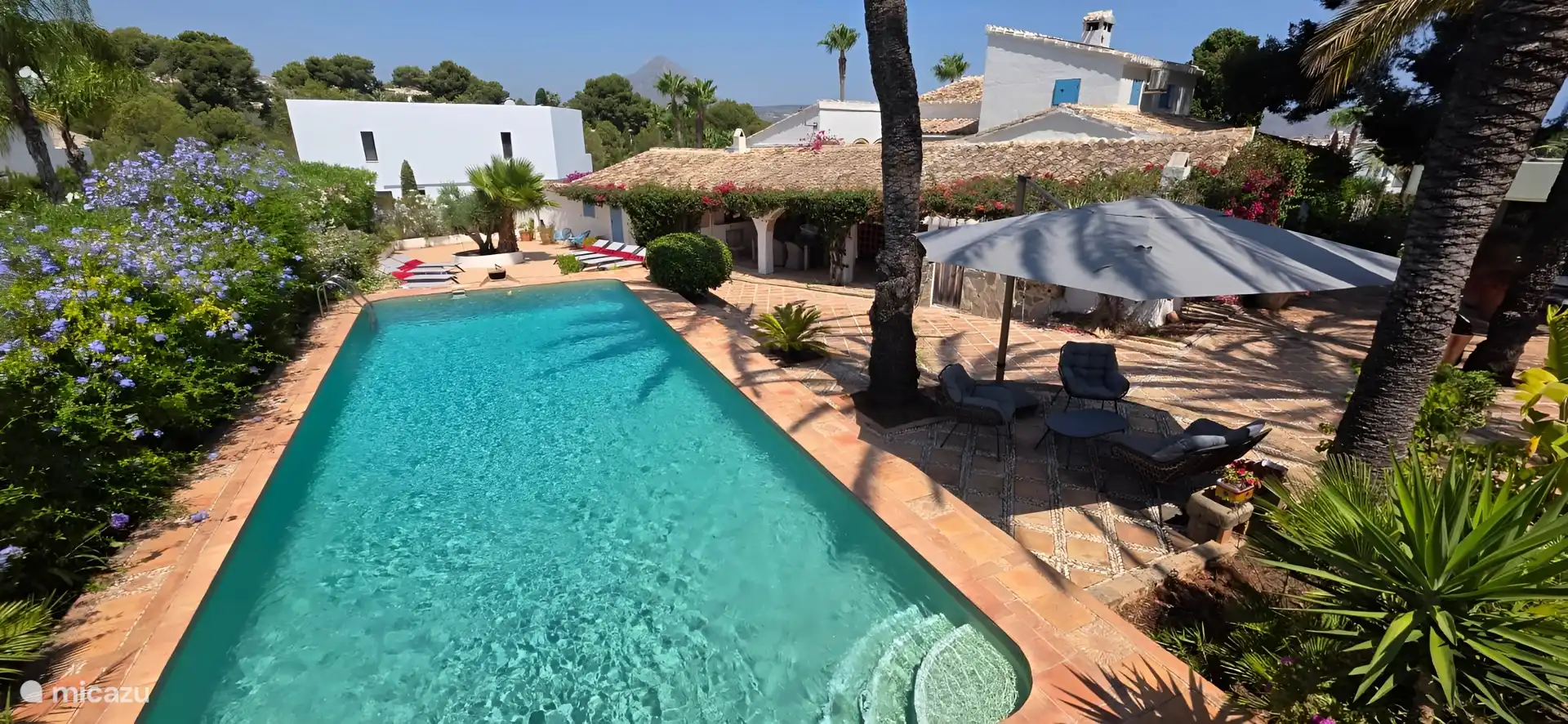 Swimming pool with sun loungers and cozy seating under the umbrella