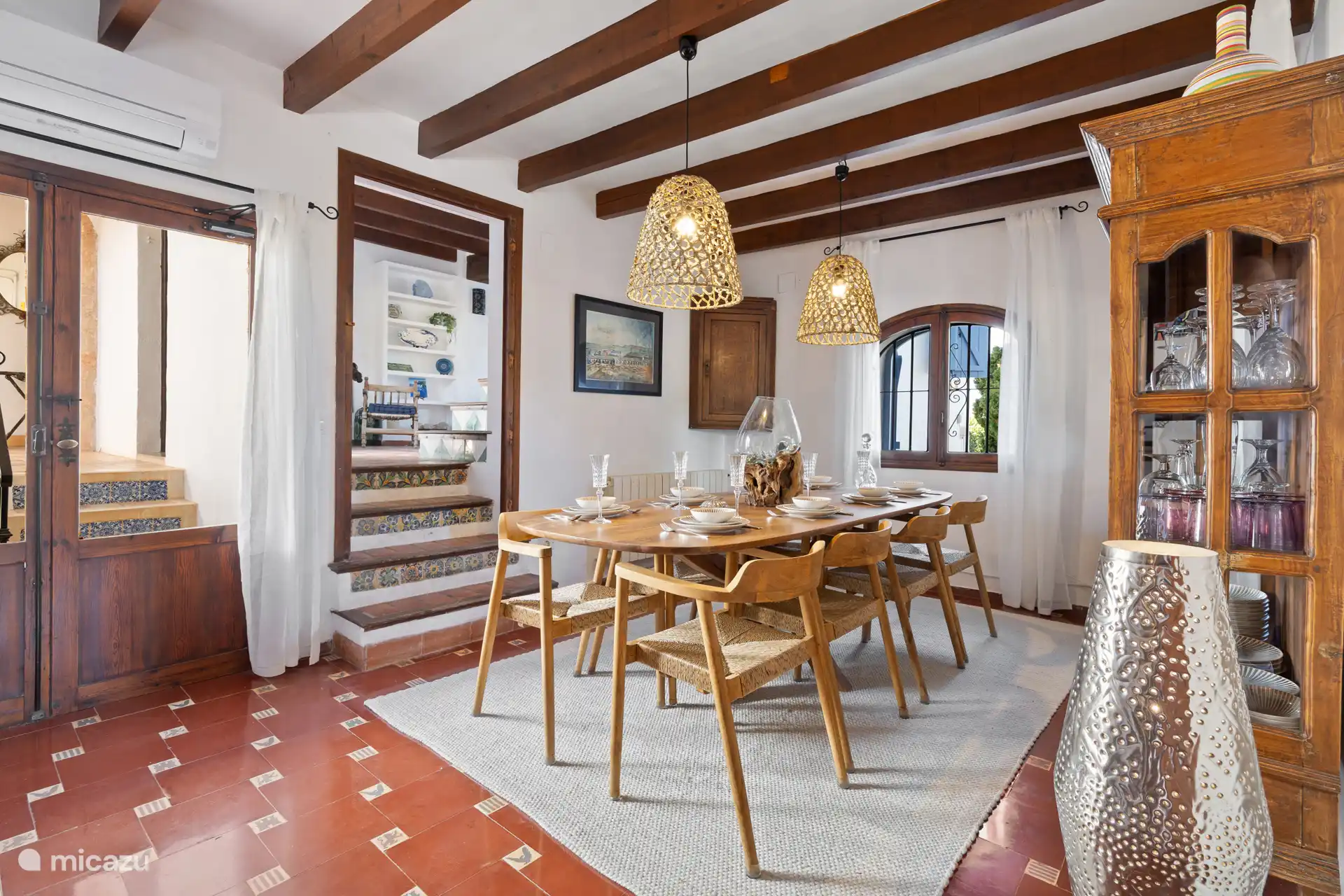 Salle à manger chaleureuse avec une grande table pour 8 personnes, une table d’échecs avec deux chaises et un authentique sol carrelé espagnol. De là, on passe au salon (à droite) et au patio (à gauche)