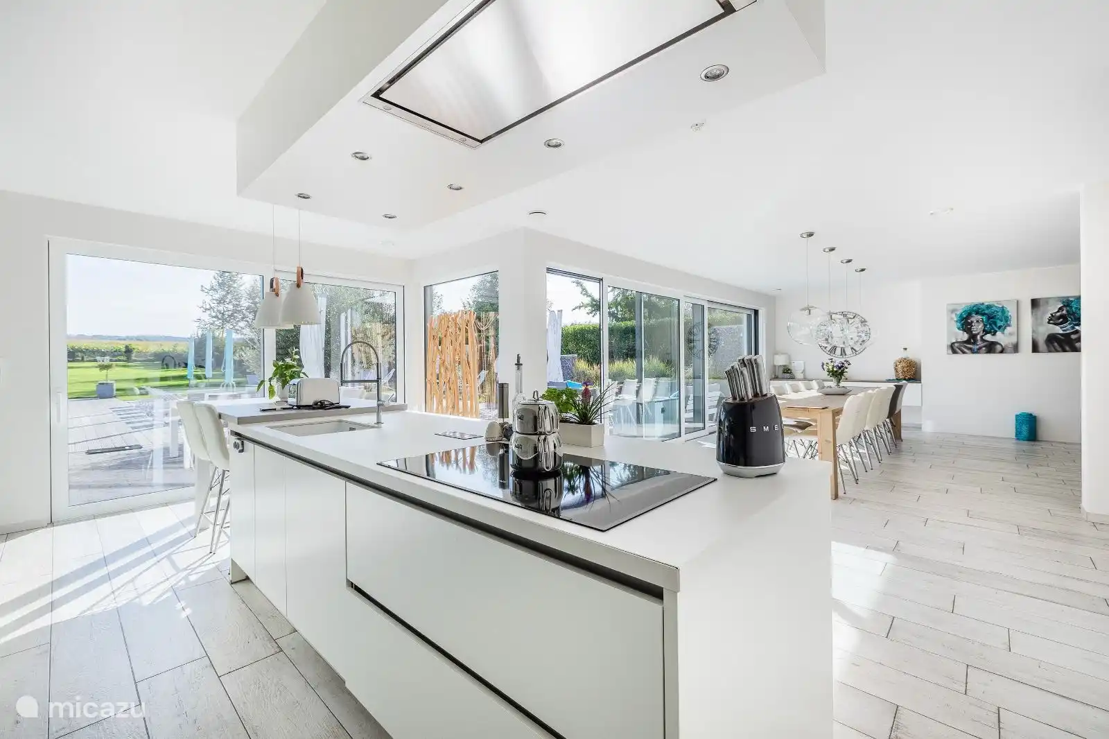 Moderna cocina abierta hiperequipada con una gran isla de cocción (4 m) y mesa de comedor alta para 4 personas. Placa de inducción con 6 zonas, lavavajillas XL, microondas combi, horno, congelador, frigorífico, vinoteca. Desde la cocina contacto directo con la mesa de comedor y vistas al jardín, terrazas y piscina.