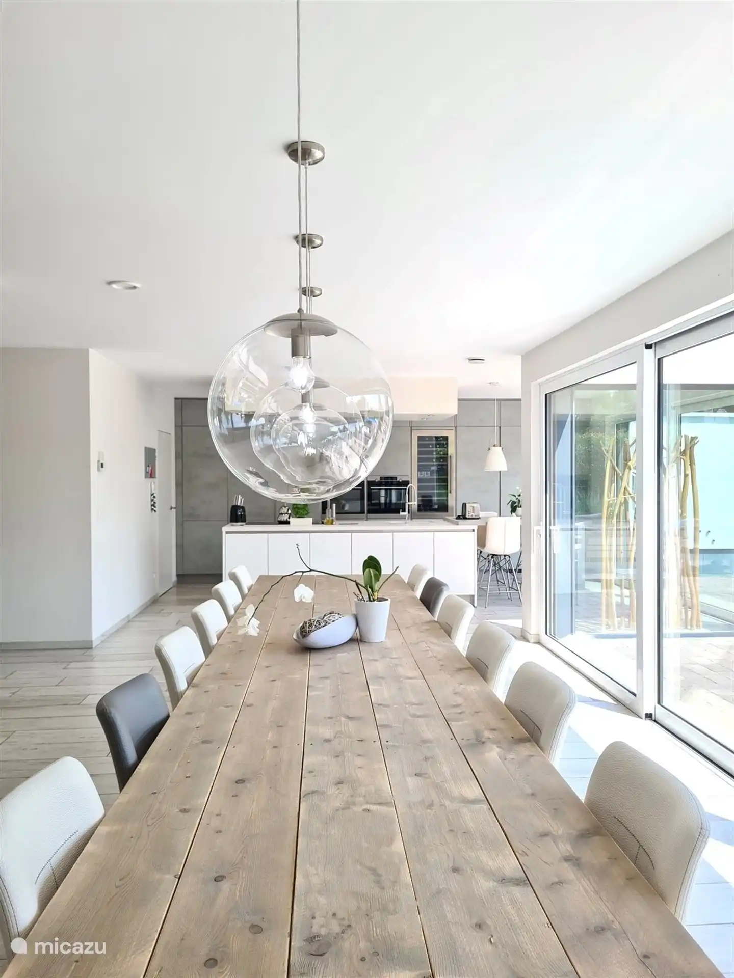 Gran mesa de comedor en salón abierto de 105m². Mesa de andamio para 14 personas. Grandes ventanas correderas para máxima luz. Vista de terrazas, jardín y piscina climatizada.