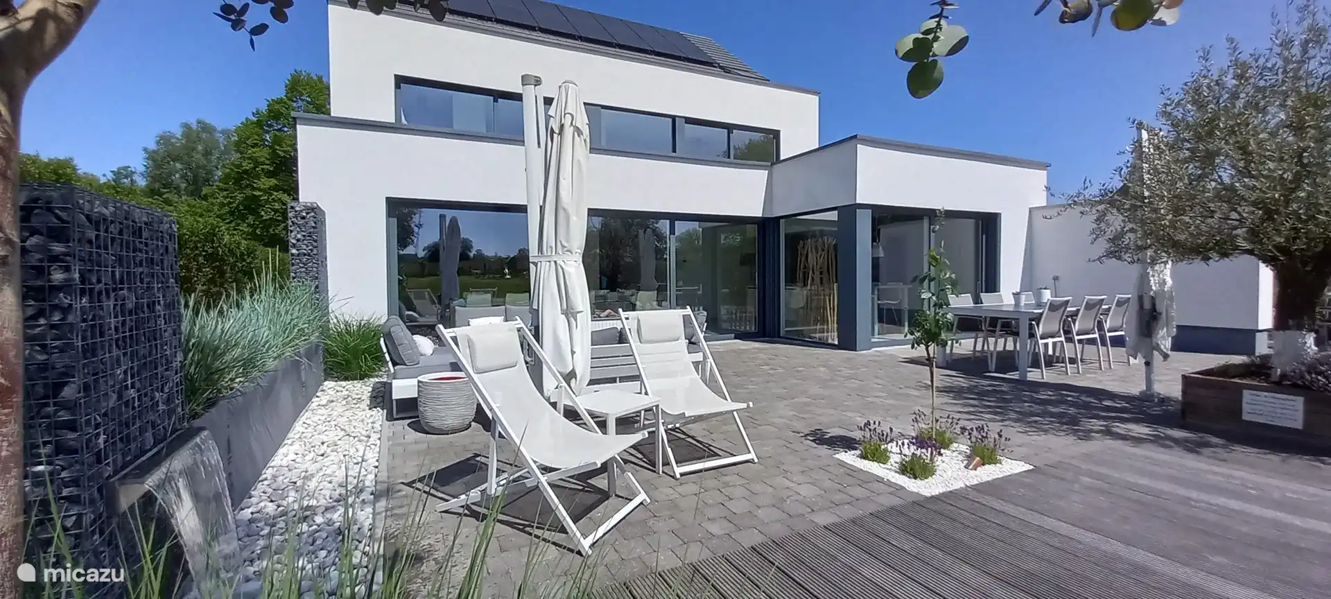 Fachada trasera grandes ventanas correderas para máxima luminosidad. Varias terrazas con zonas de estar, piscina climatizada y jardín.