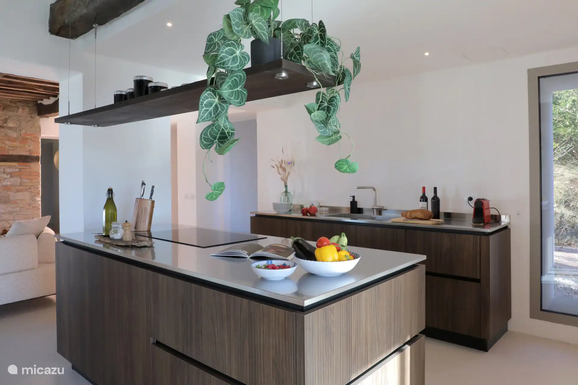 Eine moderne, offene Küche/Esszimmer mit zentraler Insel, dunklen Holzverschlüssen und rustikalen freiliegenden Balken, perfekt für das Gemeinschaftsleben.