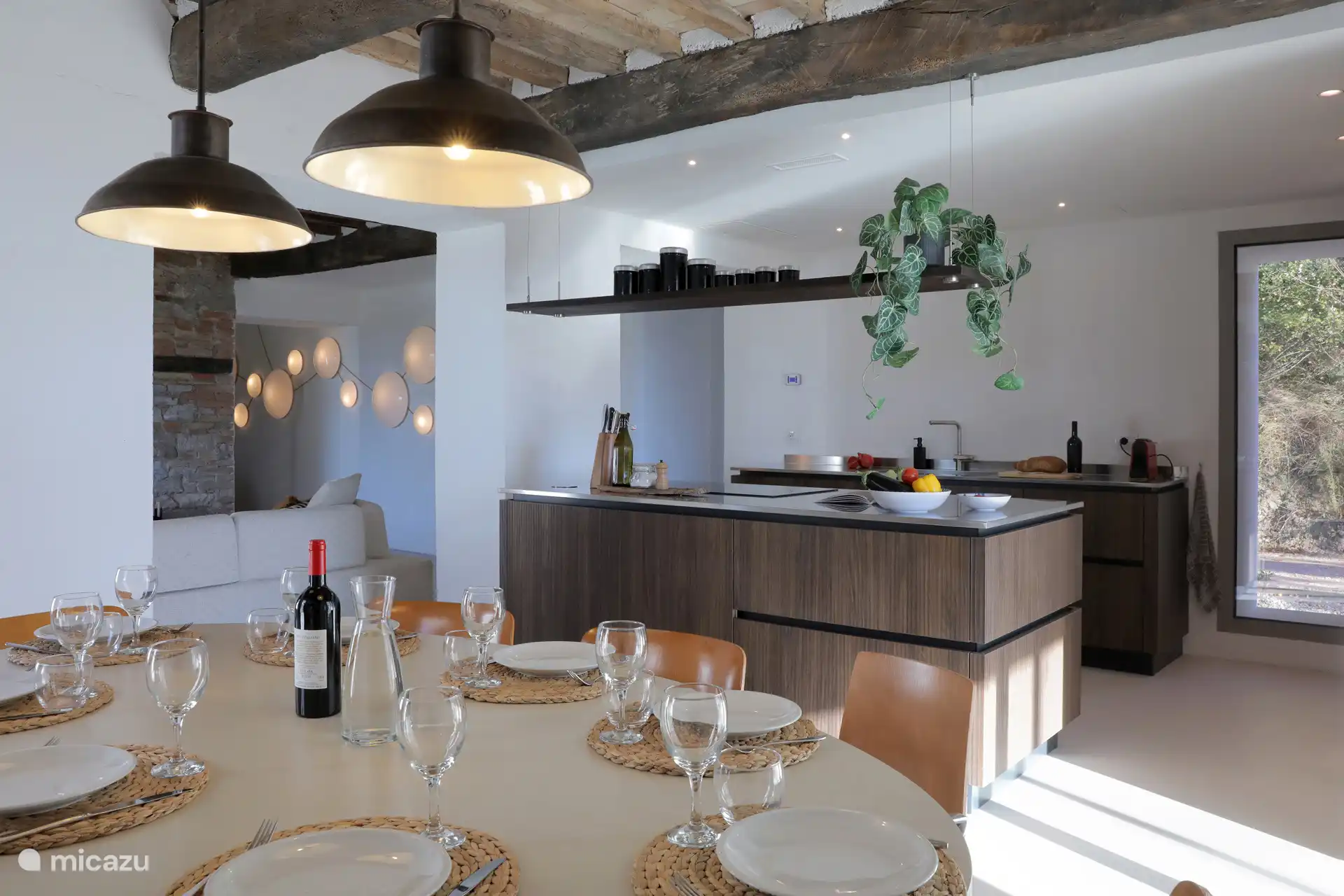 Eine moderne, offene Küche/Esszimmer mit zentraler Insel, dunklen Holzverschlüssen und rustikalen freiliegenden Balken, perfekt für das Gemeinschaftsleben.