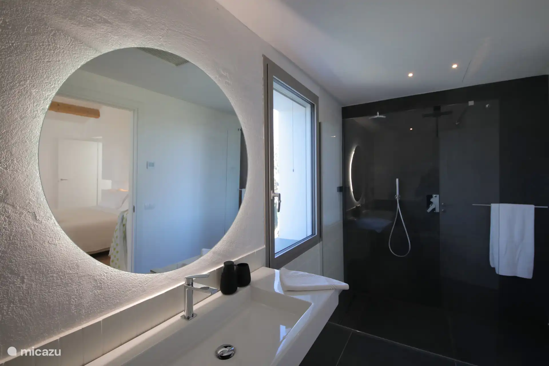 Ein modernes und elegantes Badezimmer mit Grau- und Schwarztönen. Er verfügt über einen großen hinterleuchteten Spiegel und eine geräumige begehbare Dusche mit Glaswänden.