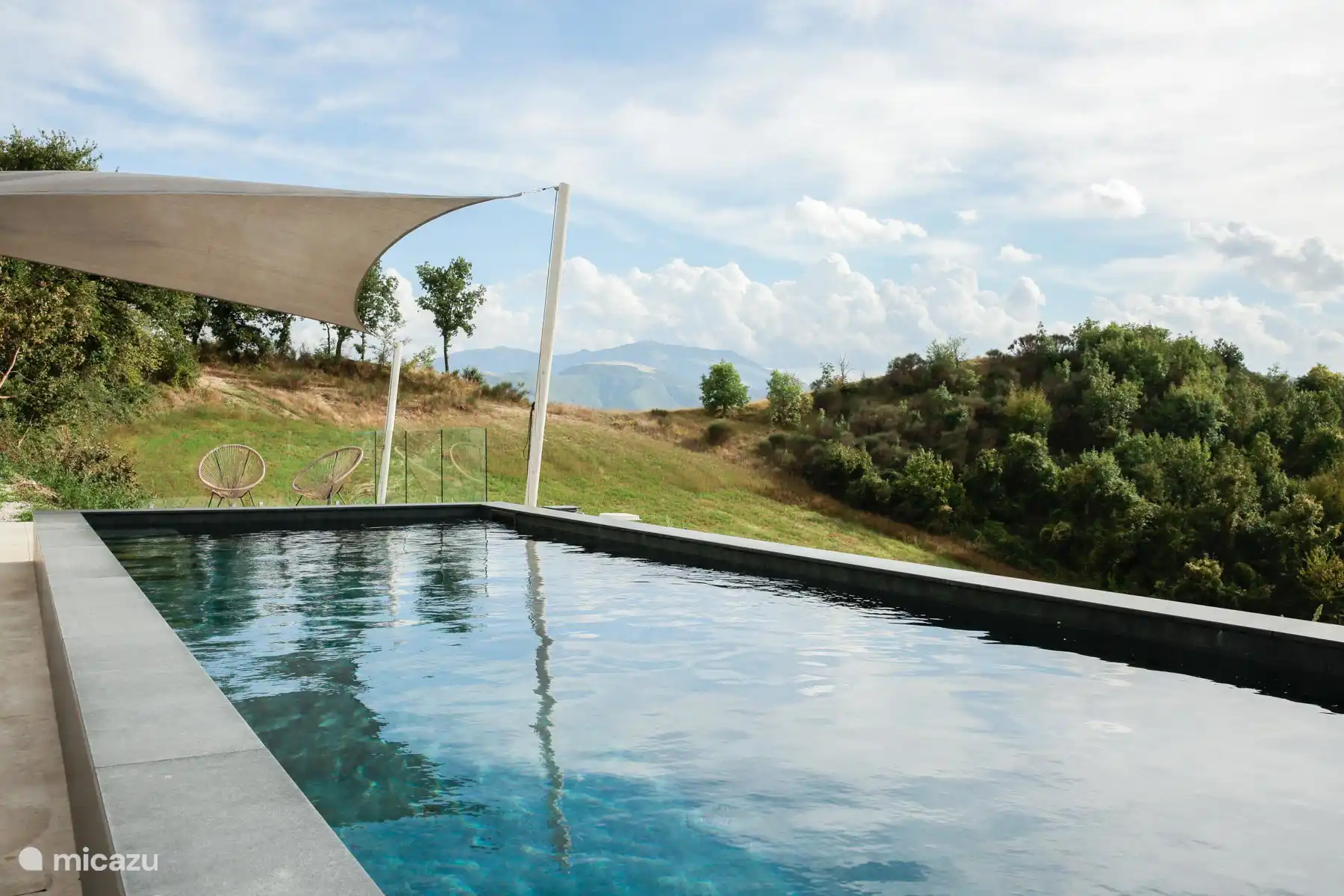 Piscine à débordement rectangulaire moderne avec une terrasse panoramique surplombant les collines, offrant des vues spectaculaires sur les Apennins.