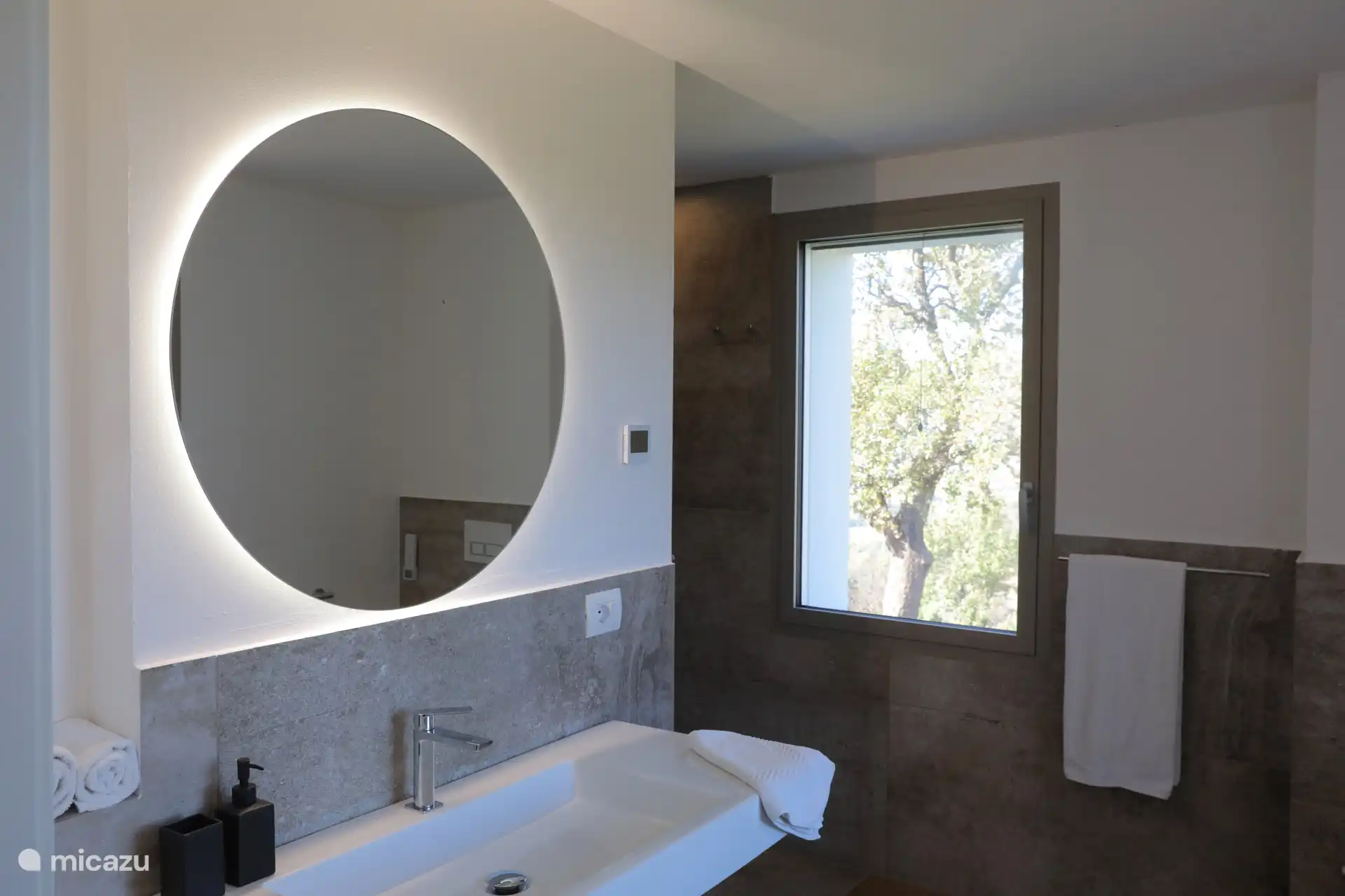 Ein modernes und elegantes Badezimmer mit Grau- und Schwarztönen. Er verfügt über einen großen hinterleuchteten Spiegel und eine geräumige begehbare Dusche mit Glaswänden.