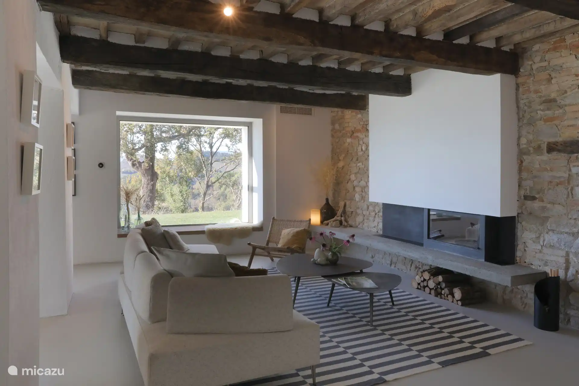 Zwei deutlich markante rustikale-moderne Wohnbereiche, hervorgehoben durch freiliegende Holzbalken, Stein-/Ziegelwände und einen zeitgenössischen Kamin. Beide Räume bieten einen großartigen Panoramablick durch große Fenster.