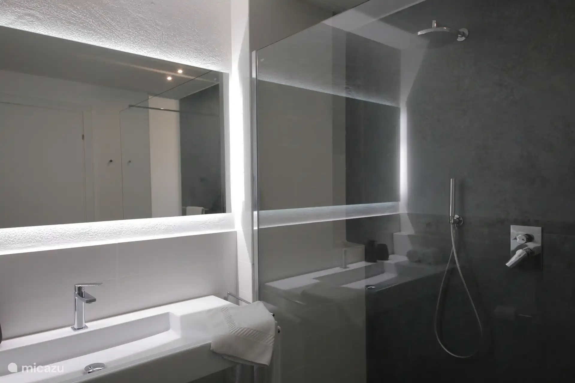 Ein modernes und elegantes Badezimmer mit Grau- und Schwarztönen. Er verfügt über einen großen hinterleuchteten Spiegel und eine geräumige begehbare Dusche mit Glaswänden.