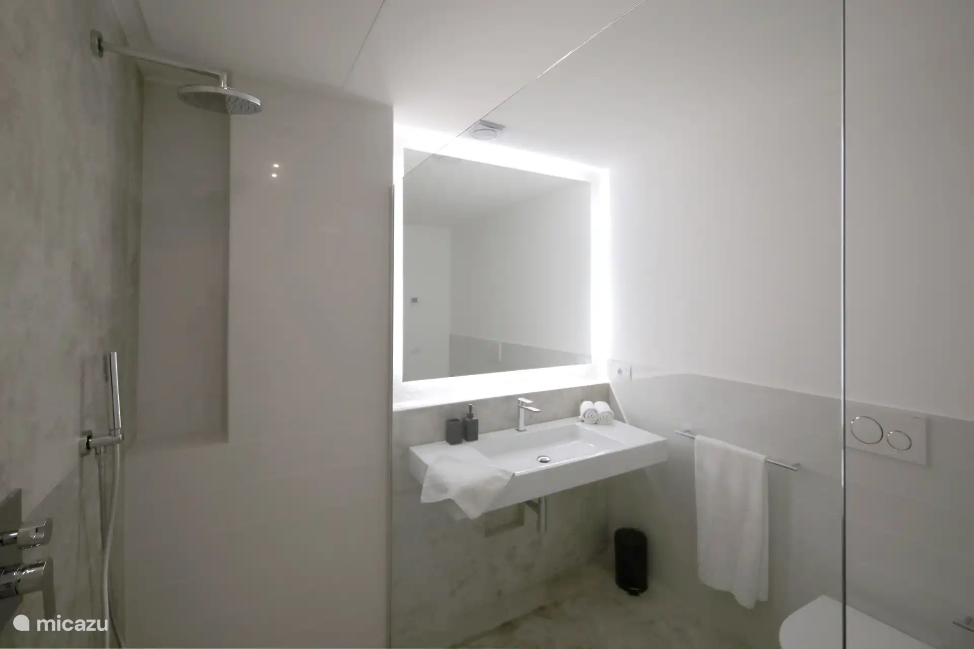 Ein modernes und elegantes Badezimmer mit Grau- und Schwarztönen. Er verfügt über einen großen hinterleuchteten Spiegel und eine geräumige begehbare Dusche mit Glaswänden.