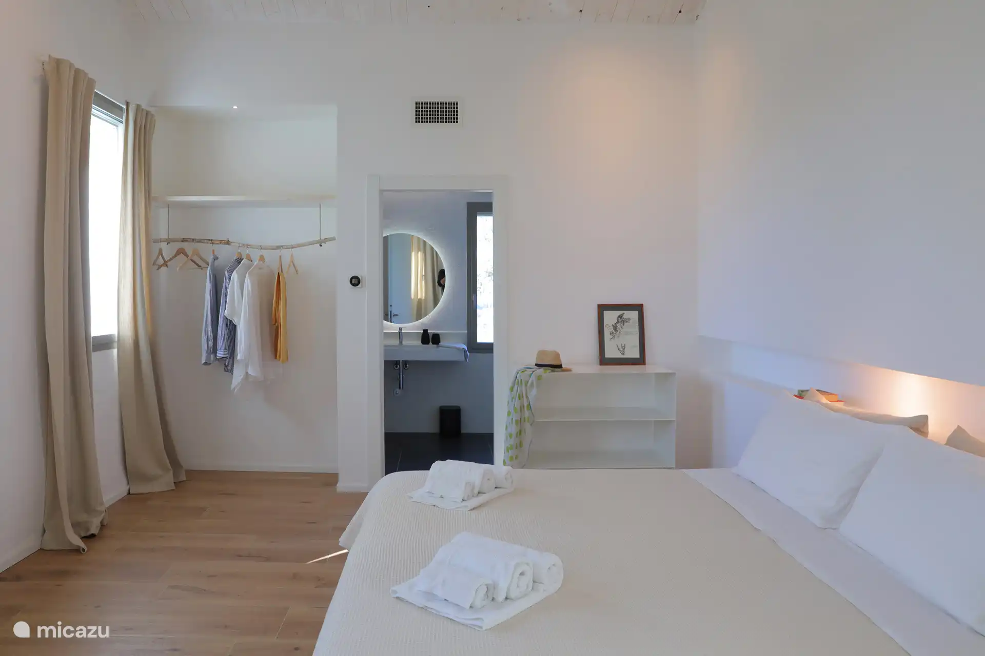 Ein helles, minimalistisches Schlafzimmer mit rustikal-schickem Flair und einer hohen geneigten Decke mit freiliegenden Holzbalken. Leichte Holzböden und weiße Wände schaffen eine luftige und entspannte Atmosphäre.