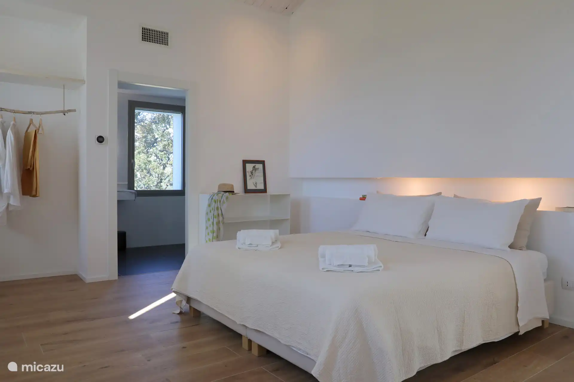 Ein helles, minimalistisches Schlafzimmer mit rustikal-schickem Flair und einer hohen geneigten Decke mit freiliegenden Holzbalken. Leichte Holzböden und weiße Wände schaffen eine luftige und entspannte Atmosphäre.