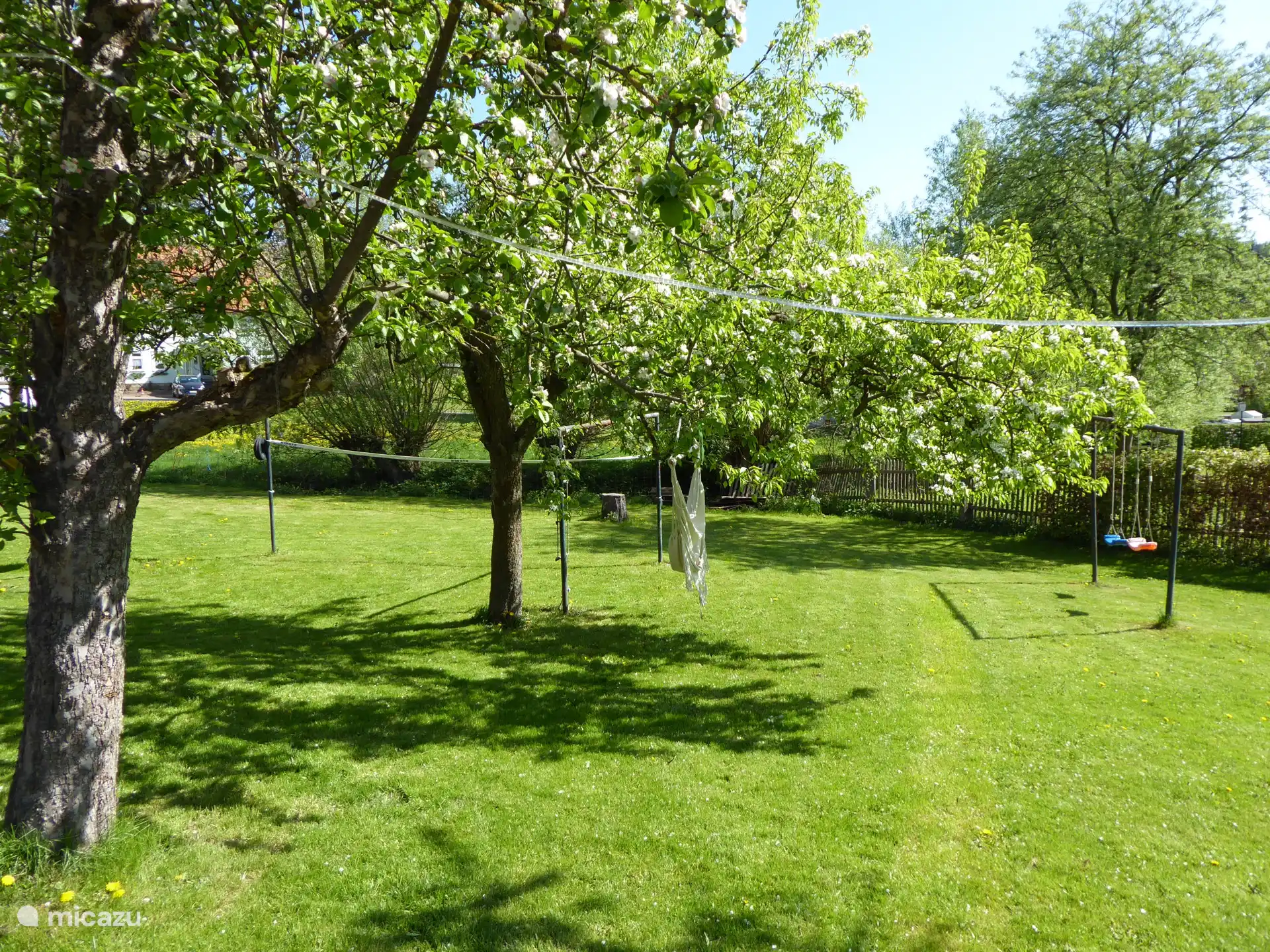 De boomgaard, met schommels, hangmat, badmintonnet en glijbaan