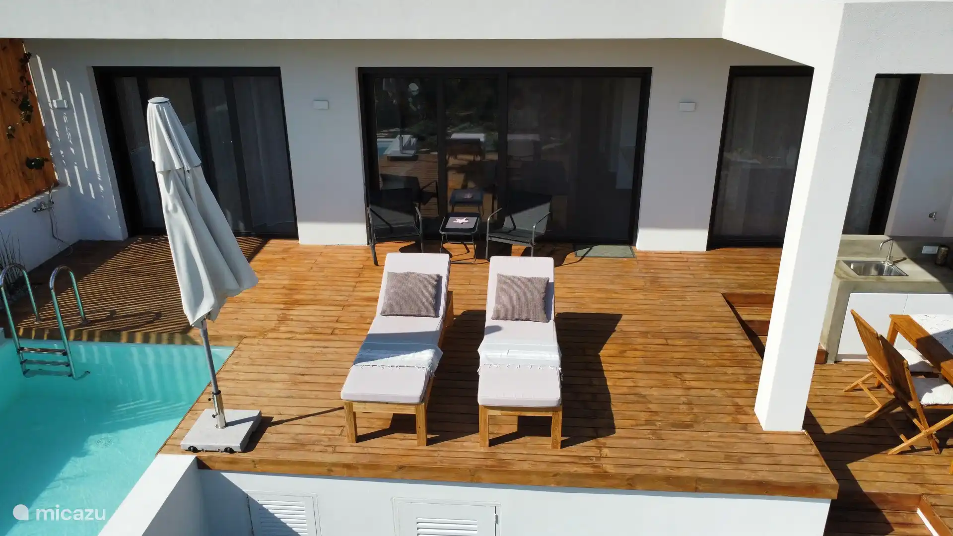 Zwembadterras met parasol en ligbanken.