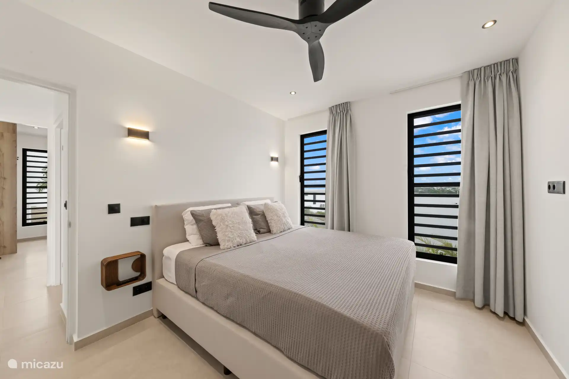 Slaapkamer met tweepersoonsbed, plafondventilator en grote ramen voor natuurlijke ventilatie.