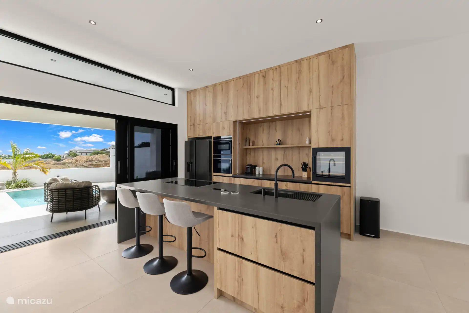 Open keuken met kookeiland, moderne apparatuur en zicht op het terras en zwembad.