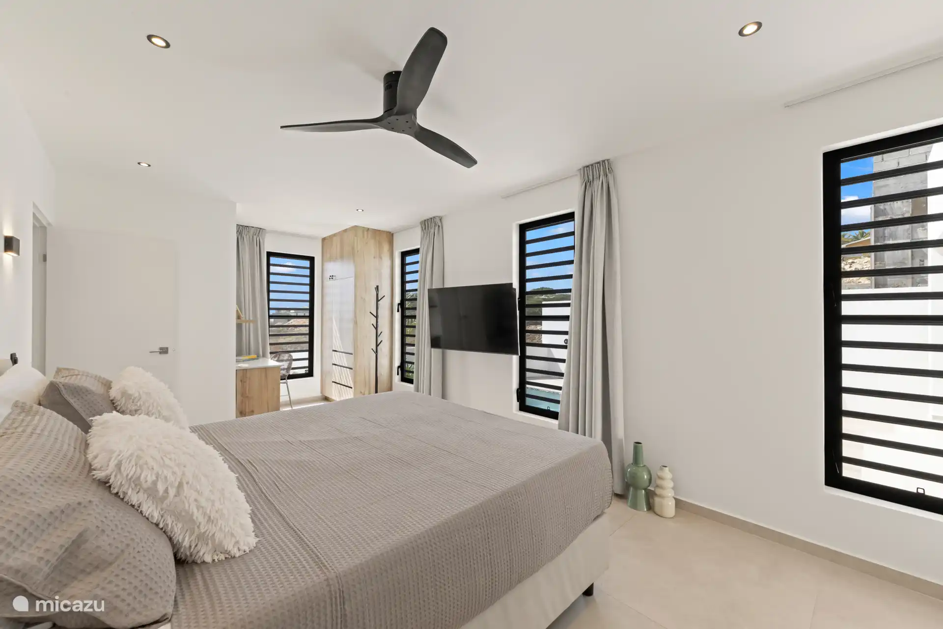 Ruime slaapkamer met tweepersoonsbed, plafondventilator, airconditioning en tv.