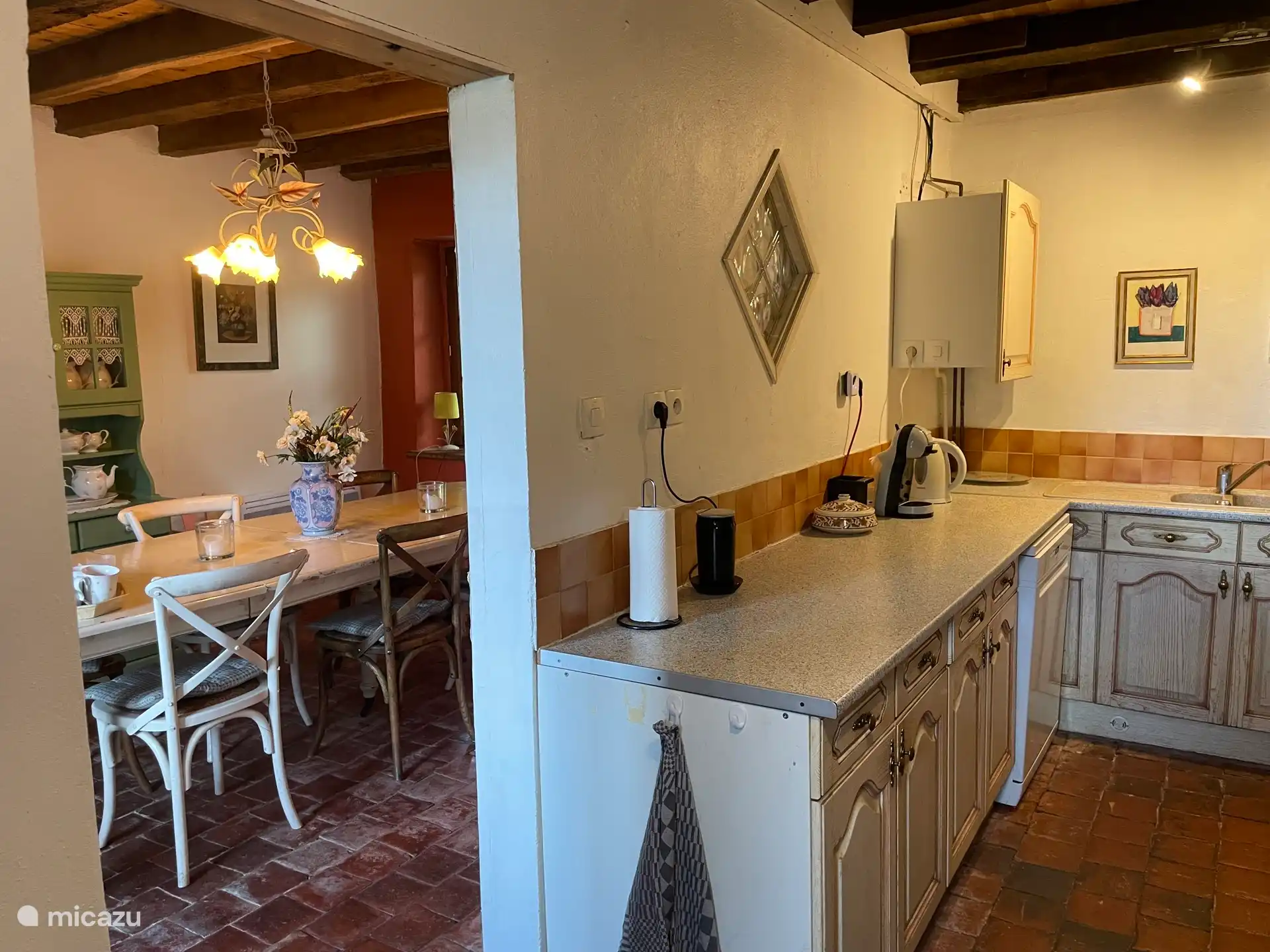 Foto von der Küche und dem Esszimmer daneben. In der Küche steht eine Kaffeemaschine mit Tassen, einem Wasserkocher und einem Milchaufschäumer.