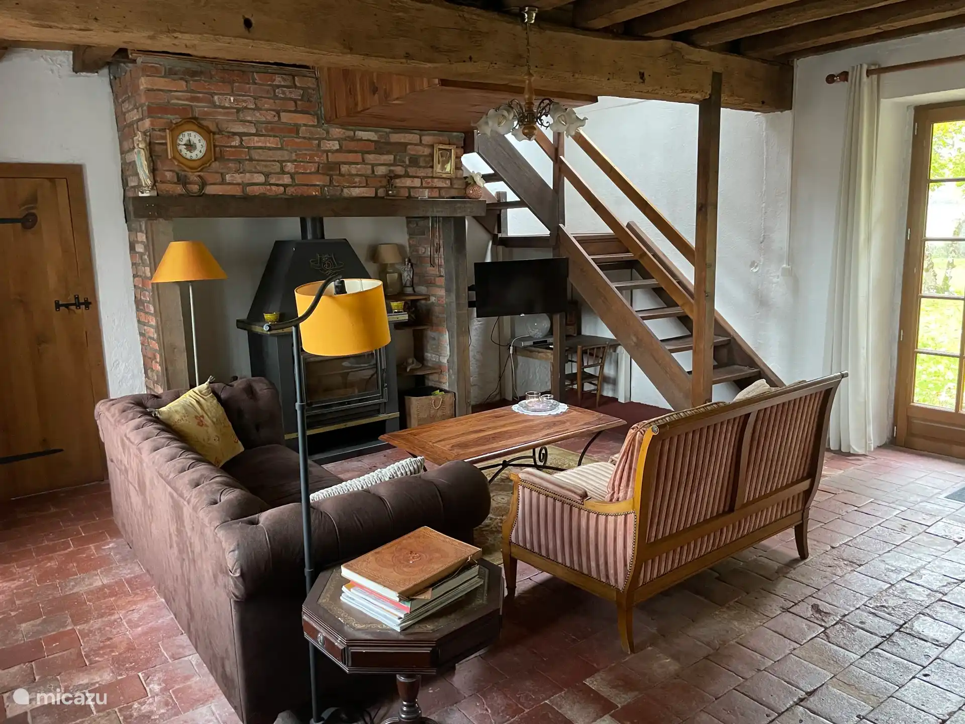 Sitzgelegenheiten im Salon mit Holzofen und Treppen nach oben. Links ist die Tür zum Hauswirtschaftsraum sichtbar.