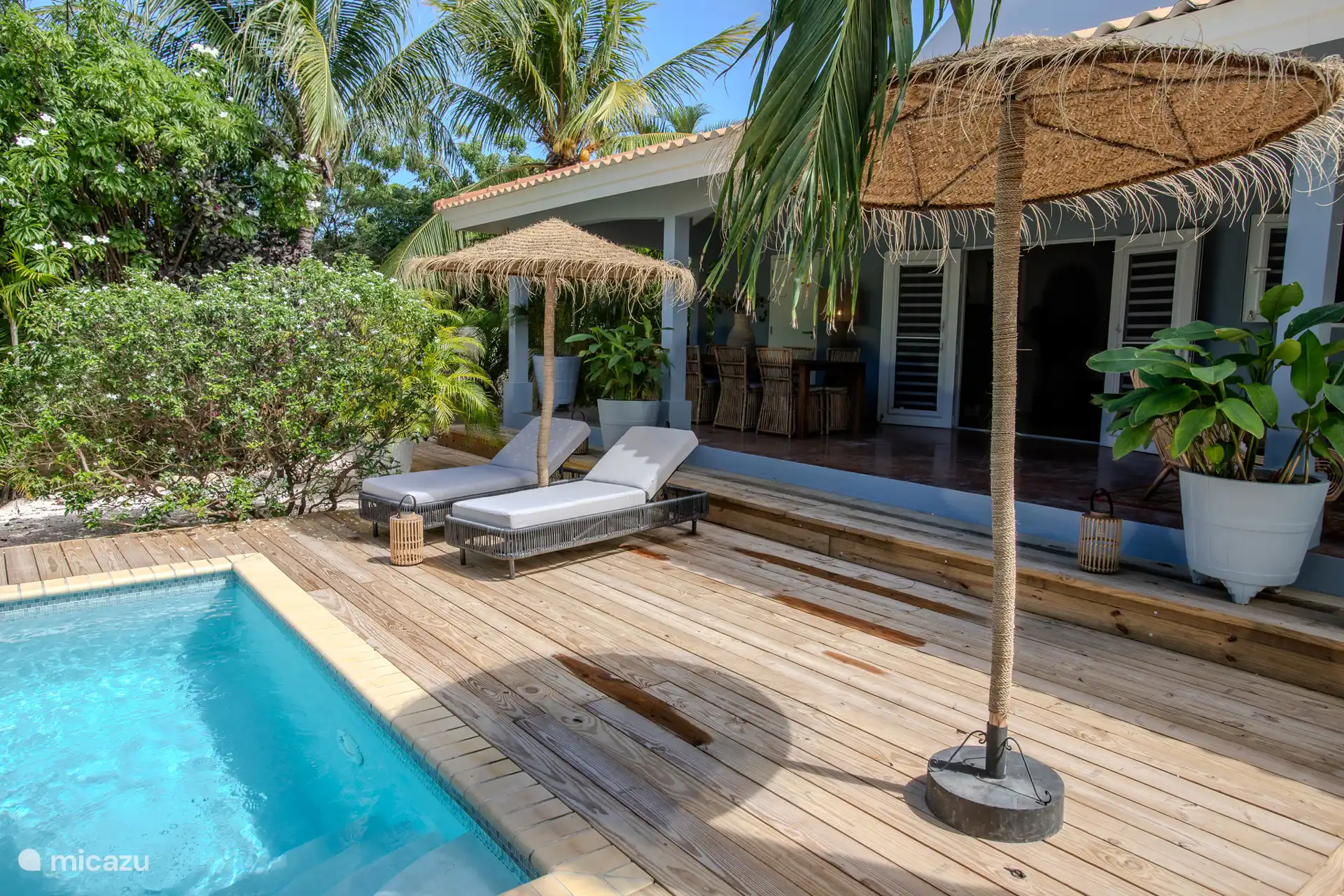 2 preciosas tumbonas bajo una sombrilla de paja junto a la piscina, con una bebida y un tentempié, y disfruta del precioso jardín tropical