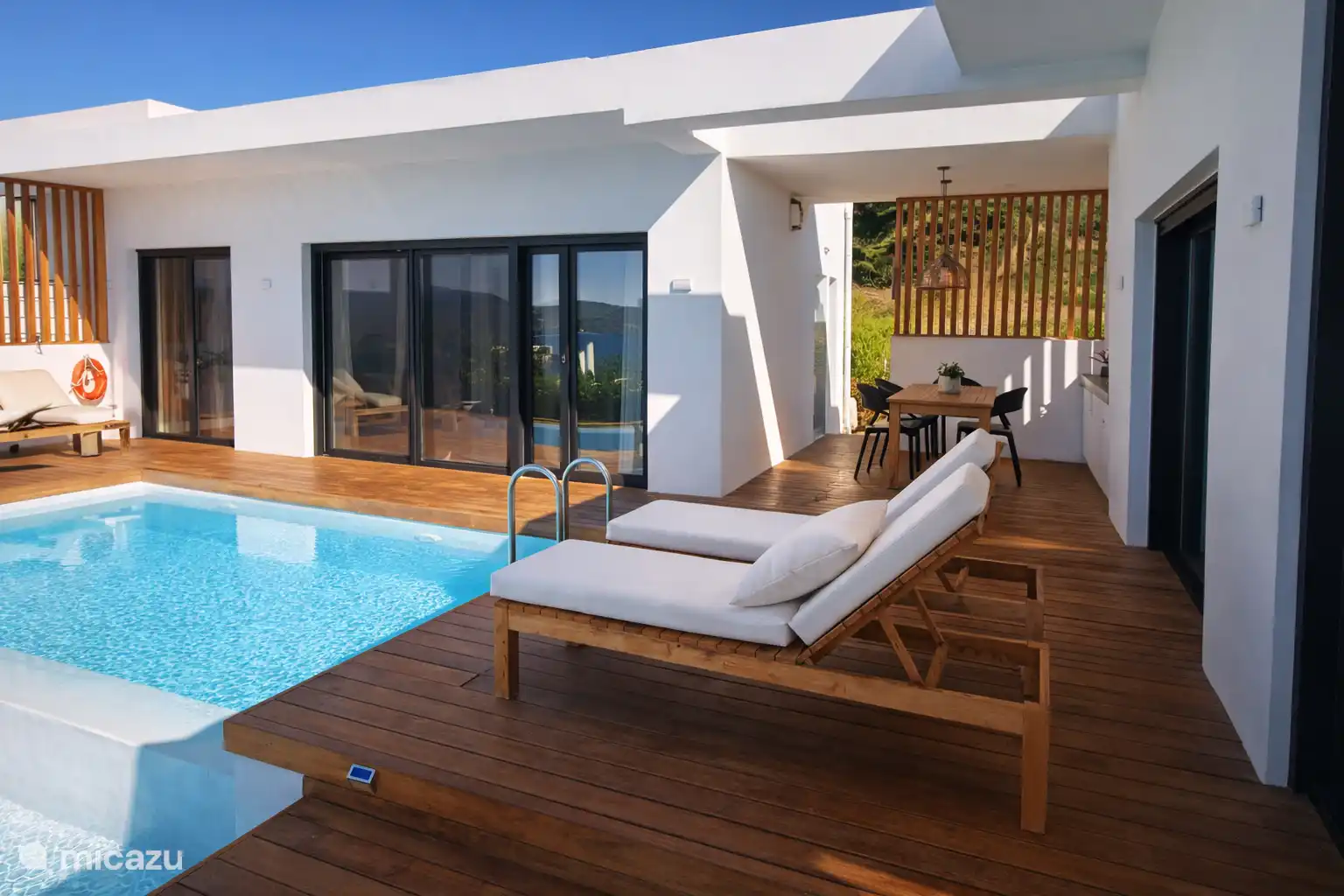 La terrasse avec les pièces gest à droite et le bâtiment principal avec la chambre principale, la salle de bain attenante et le salon/cuisine à gauche de la photo 