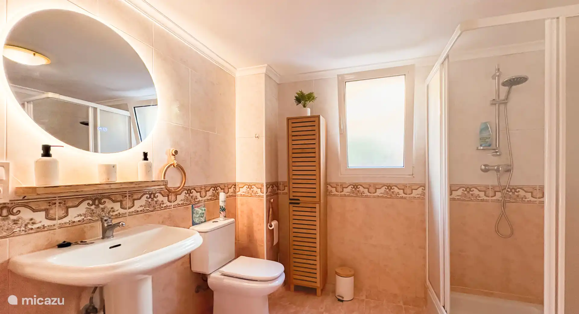 Badkamer met wastafel, spiegel, WC en kastje, wasmachine en grote extra koelkast/vrieskast.